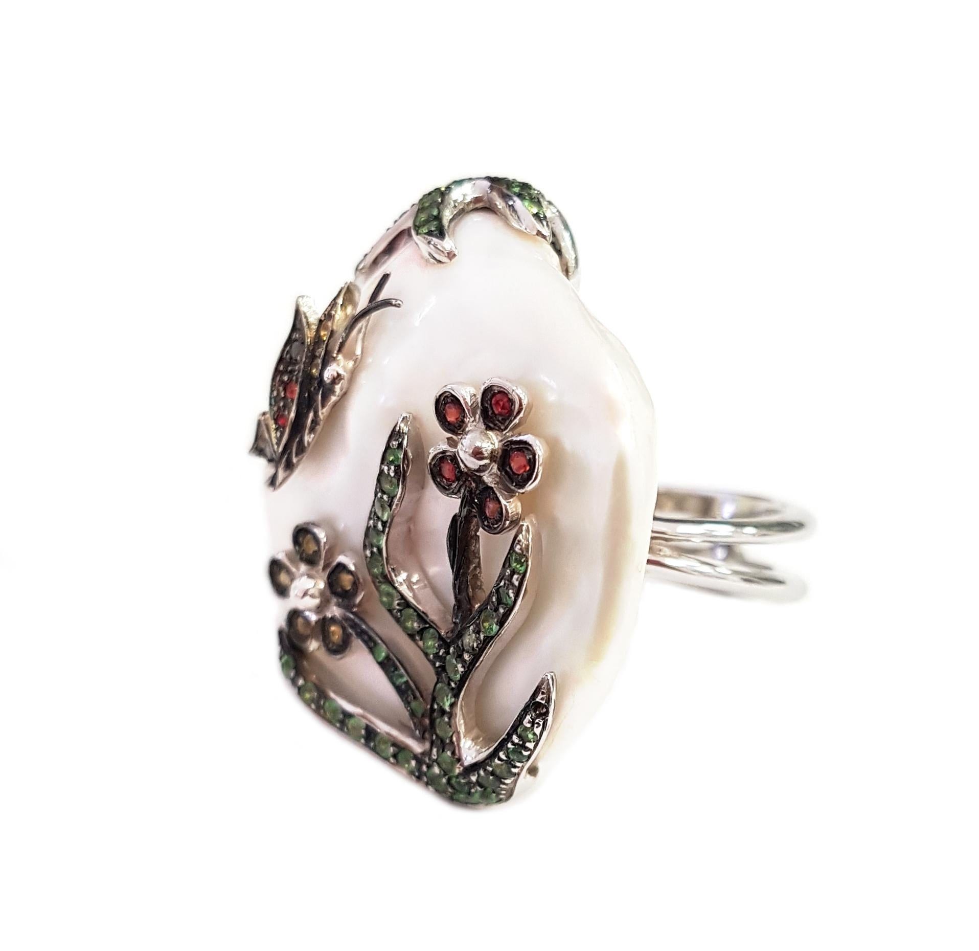 This gorgeous cocktail ring features a large luminous freshwater pearl, sapphires and tsavorites. A charming pastoral scene of spring plays out on the surface of the pearl; under the branch of a tree, bright green with new leaves, a butterfly flits