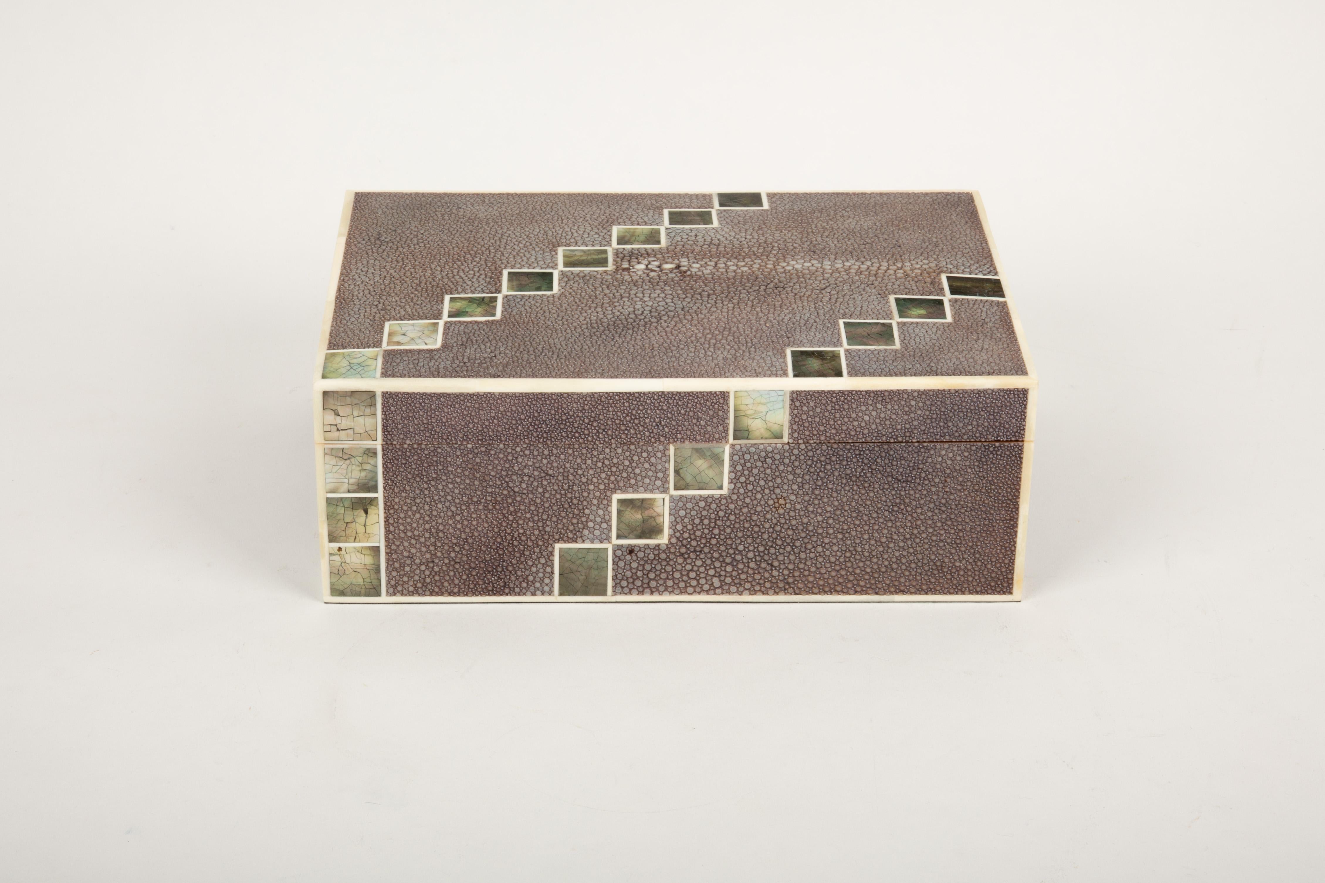This exquisite Mother of Pearl and Shagreen box is a true masterpiece of craftsmanship, measuring 7.25” x 10” x 3.75”H. Handcrafted in the Philippines by master artisans, it features a stunning combination of luxurious shagreen and luminous