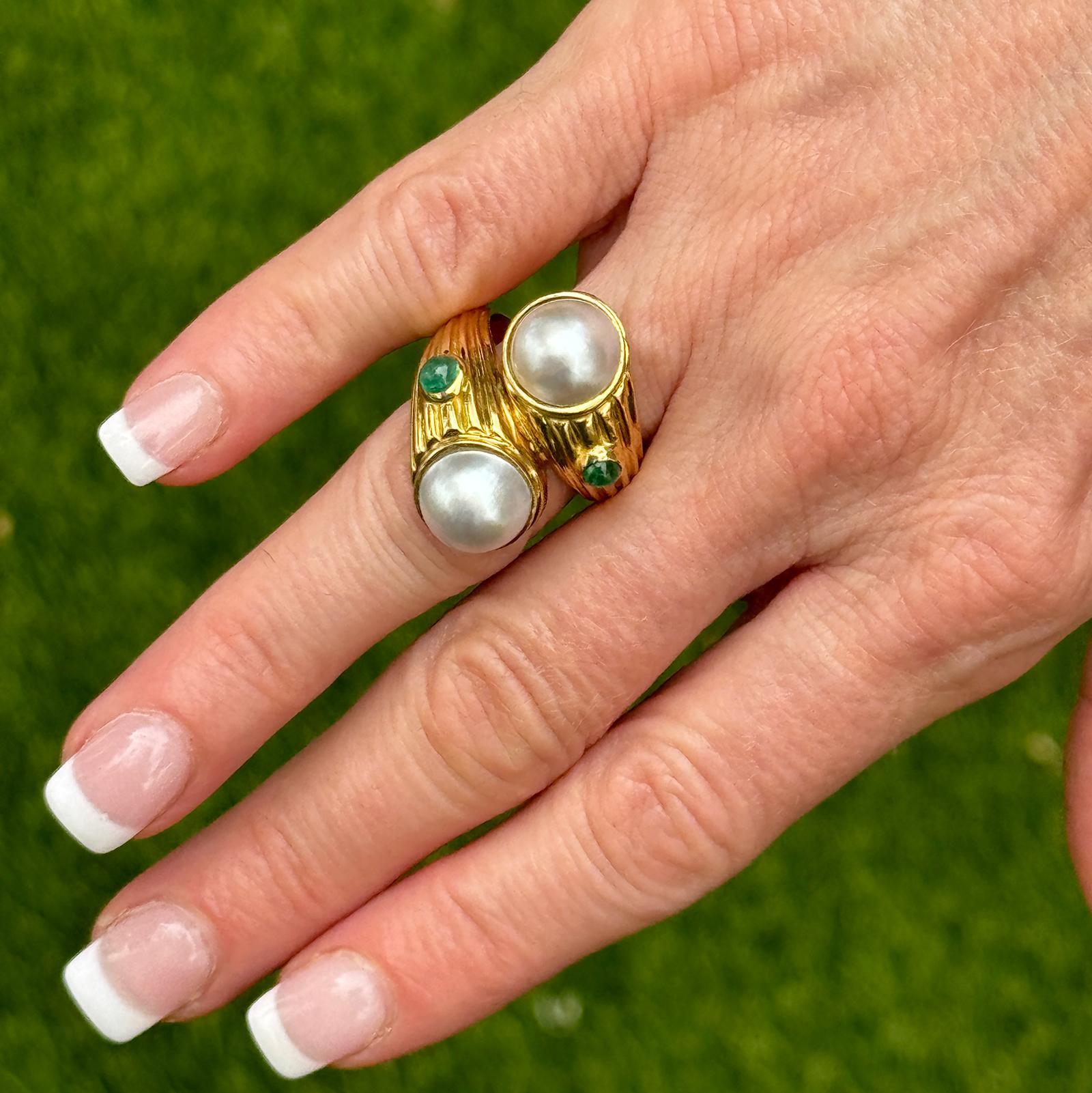 Pearl and emerald vintage bypass ring handcrafted in ribbed 18 karat yellow gold. The ring features two 10mm cultured pearls and 2 bezel set emerald accents. The ring measures 15mm in front in width, and is currently size 7 ( can be sized). Weight: