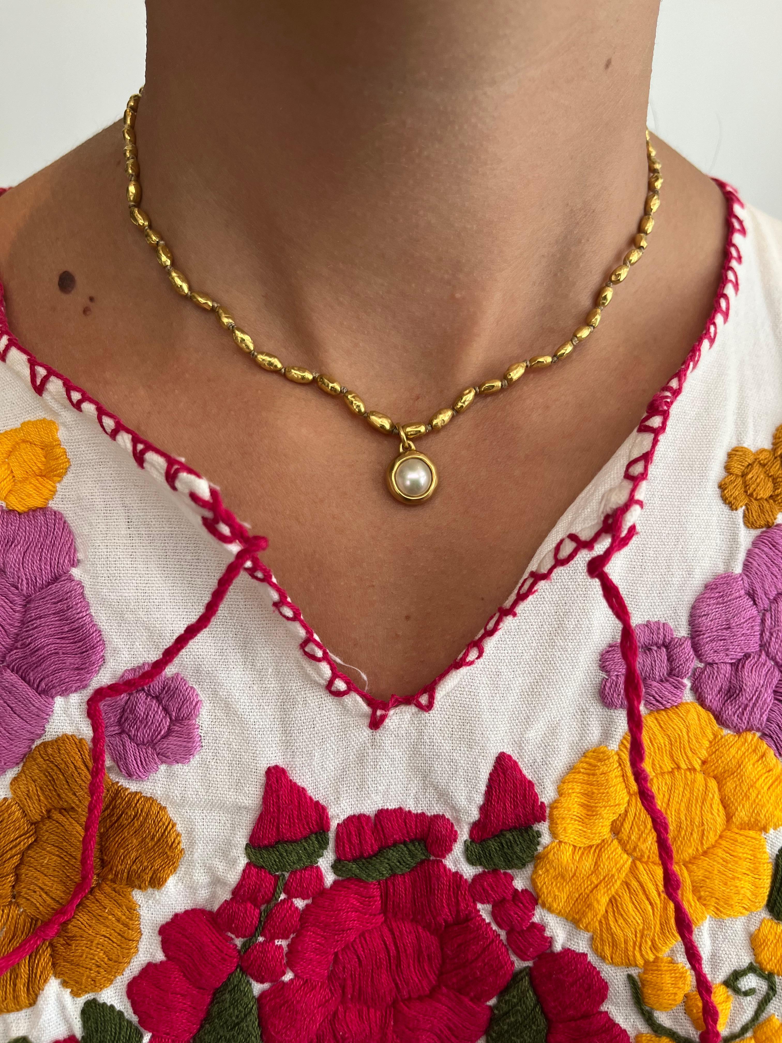 A bezeled pearl pendant-charm wrapped in 22K yellow gold, handmade by Bracken Jewelers in Los Angeles, California. The luminous rounded pearl is framed in rich high karat gold with a raw hammered finish, emphasizing its soft luster and organic