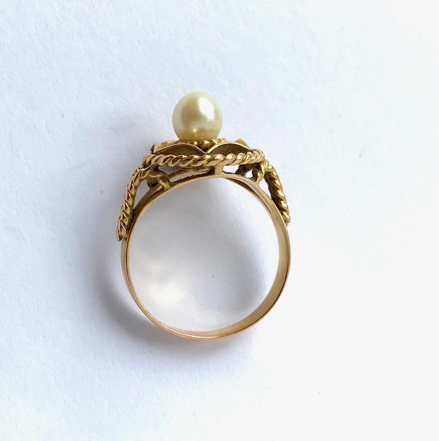 Vintage Ring aus 18 kt Gelbgold und einer Perle um 1960
Eine Zuchtperle Durchmesser 5 mm in der Mitte eines Korbes. 
Der Korb und der obere Teil des Rings sind gedreht. Sehr guter Allgemeinzustand für dieses Schmuckstück.
Adlerkopfpunze (750/000