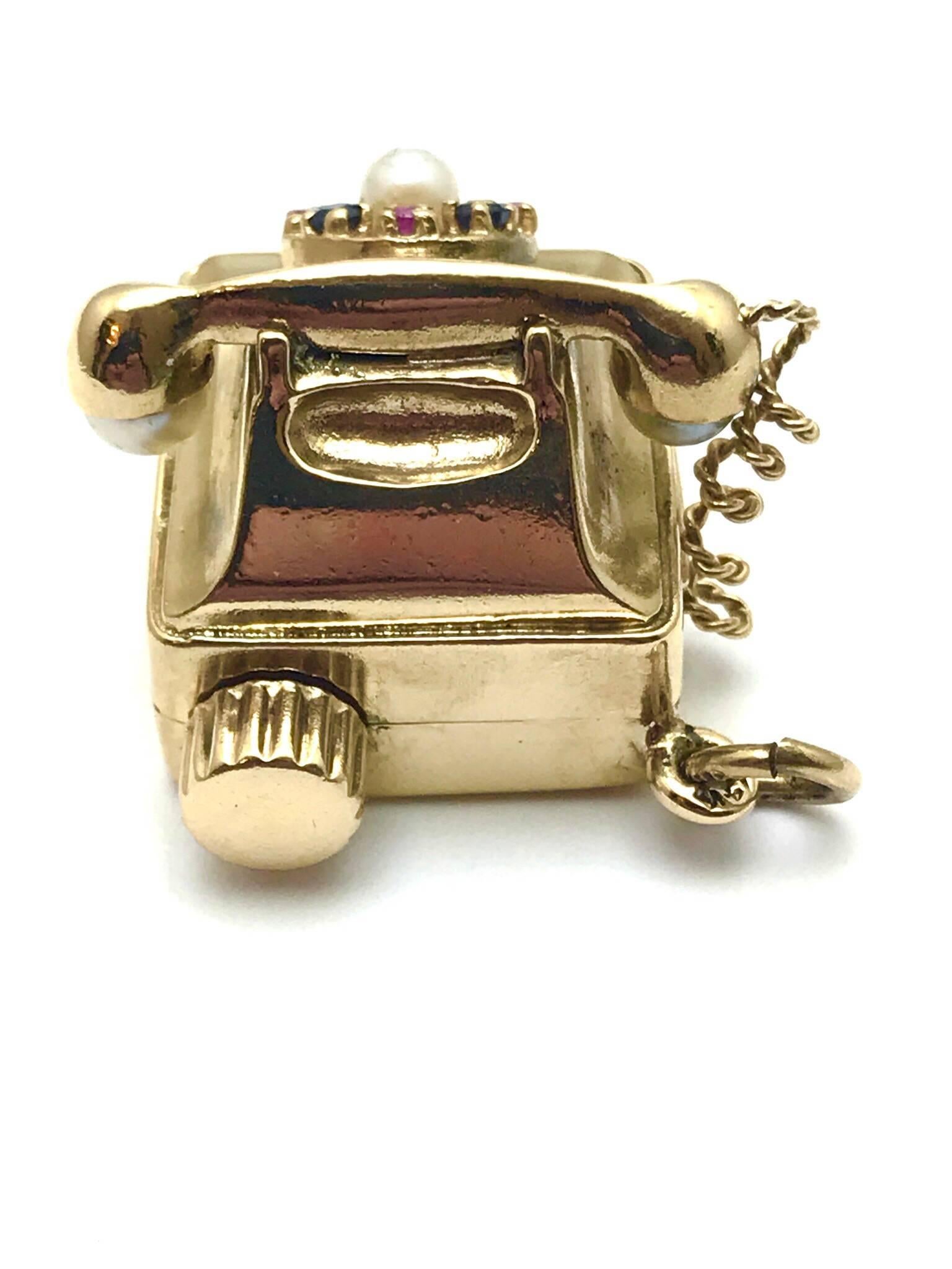 A pearl ruby and sapphire 14 karat yellow gold musical rotary phone charm presented by Charles Schwartz & Son.  The round cut rubies and sapphires along with a single pearl make up the dial of the phone, with two more pearls on the speaker and