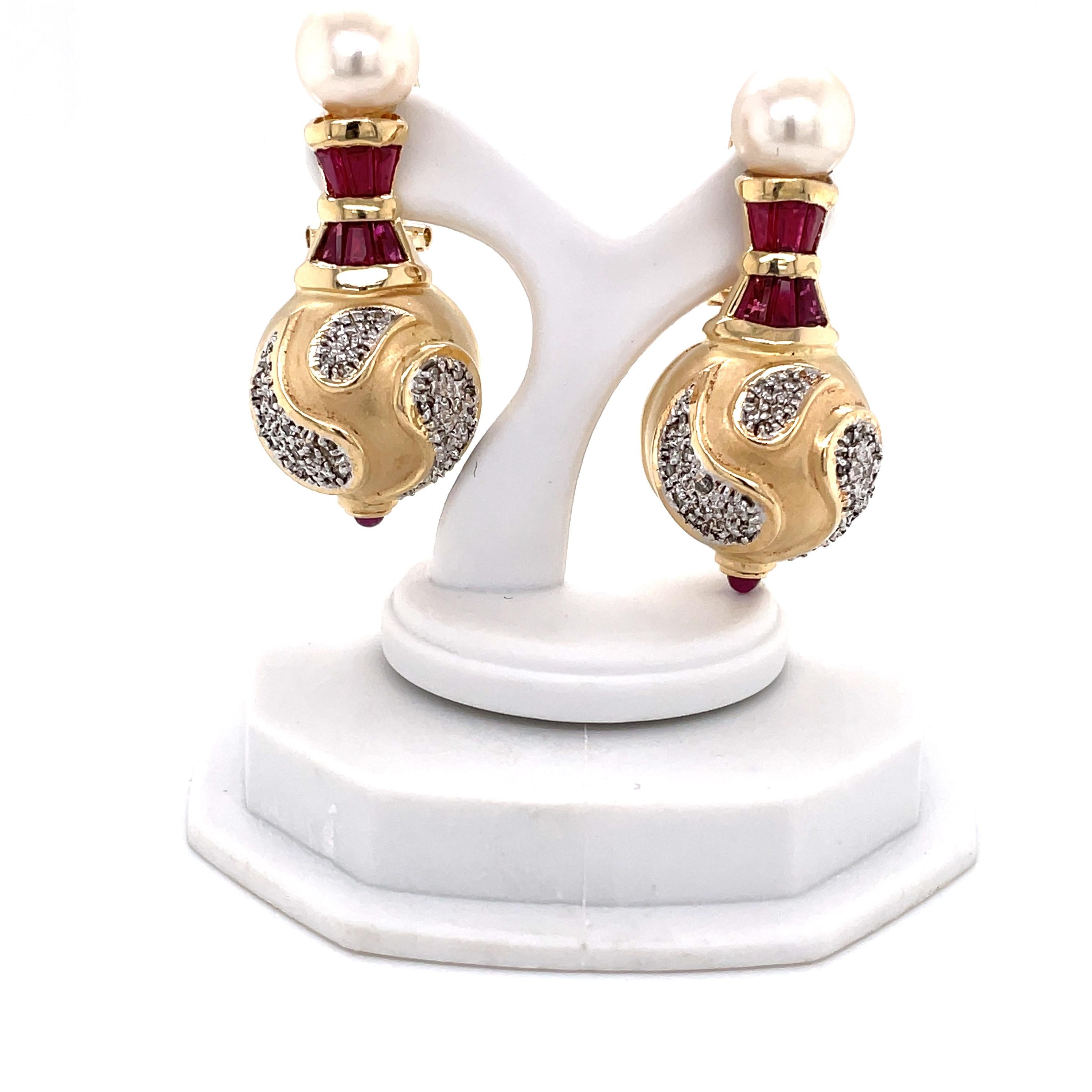 Two 8.5mm AAA round Akoya Pearl studs with tiny rubies crown this Renaissance style fourteen karat 14K yellow gold pair of drop earrings. These elegant baubles
are artfully accented with diamond tear drop swirls. Each earring measures 1-1/2 inch in