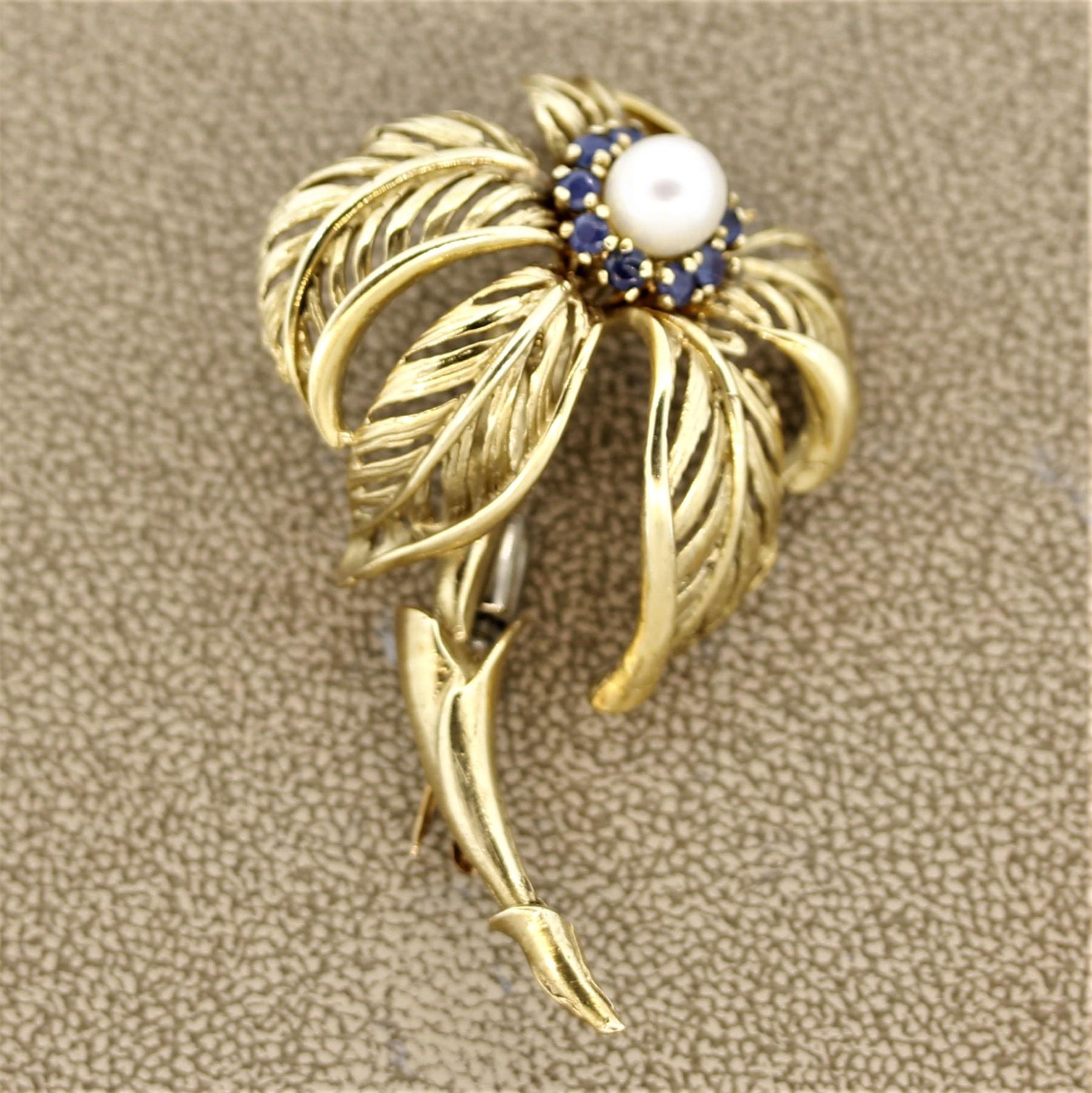 A lovely palm tree blowing in the wind. This brooch features a 7mm round Akoya pearl along with round shaped blue sapphires. The hand-sculpted brooch is made in 14k yellow gold and has excellent detail in the palm's curved leaves and elongated