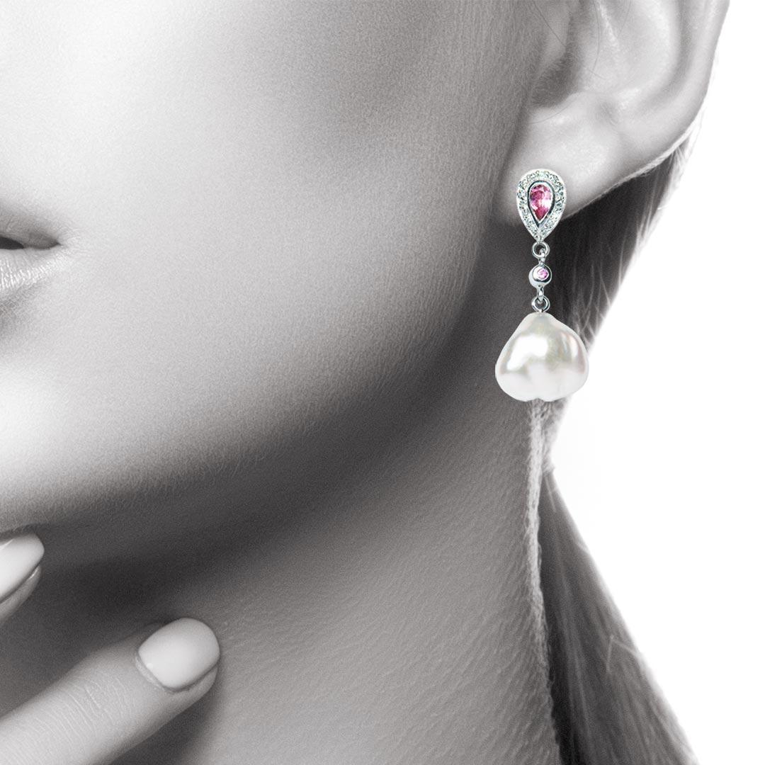 These exclusive drop earrings have a very Art Deco look. They feature pear shaped pink tourmalines set with a surround of grain set diamonds, round pink sapphires and very white Keshi Pearls. A unique pair which could not be made again. The diamond