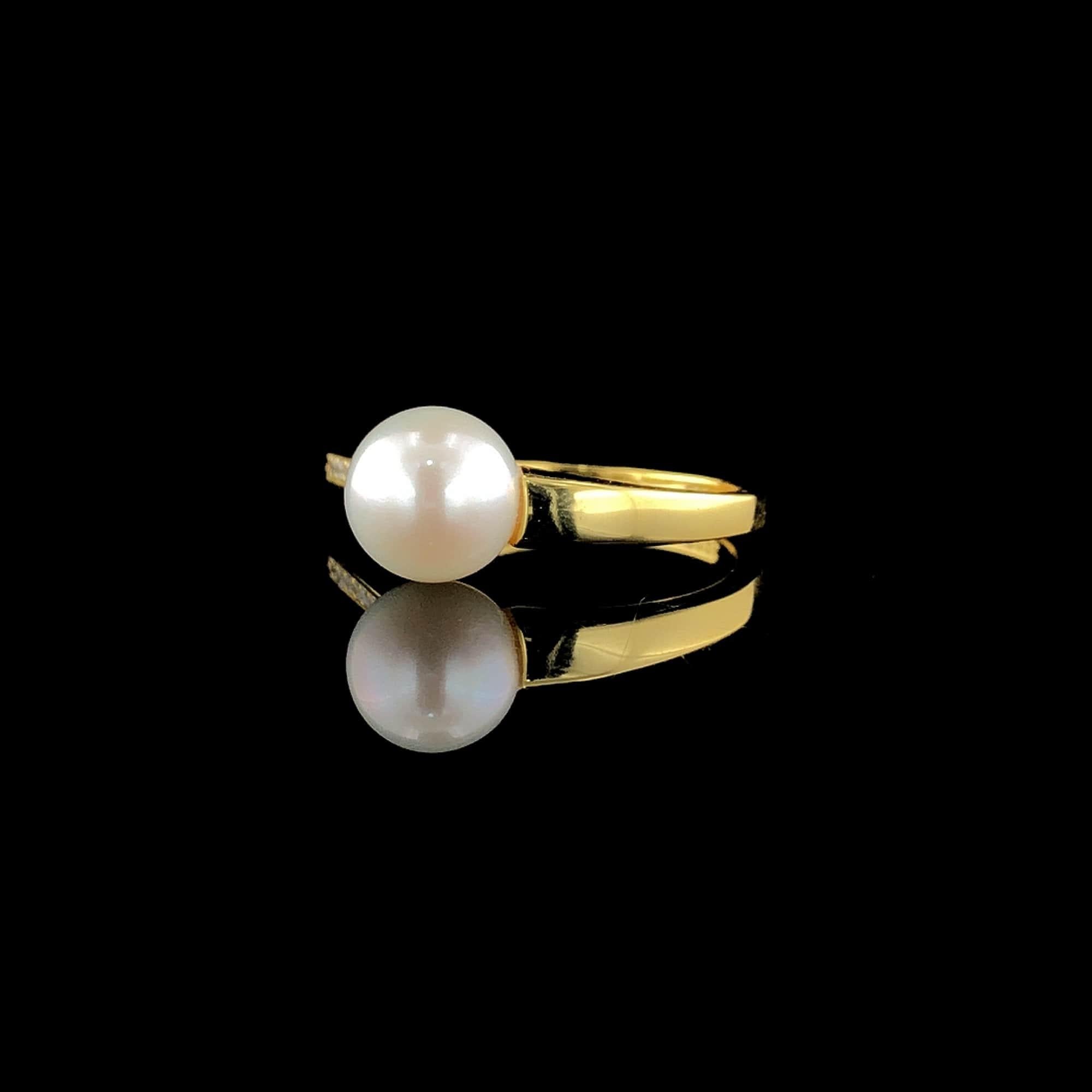 Une bague ouverte, plaquée en or 14k sur argent sterling, arbore une perle d'eau douce blanche singulière à une extrémité et une ligne rayonnante de diamants à l'autre. Ce design symbolise l'entrelacement de deux âmes, la perle incarnant la pureté