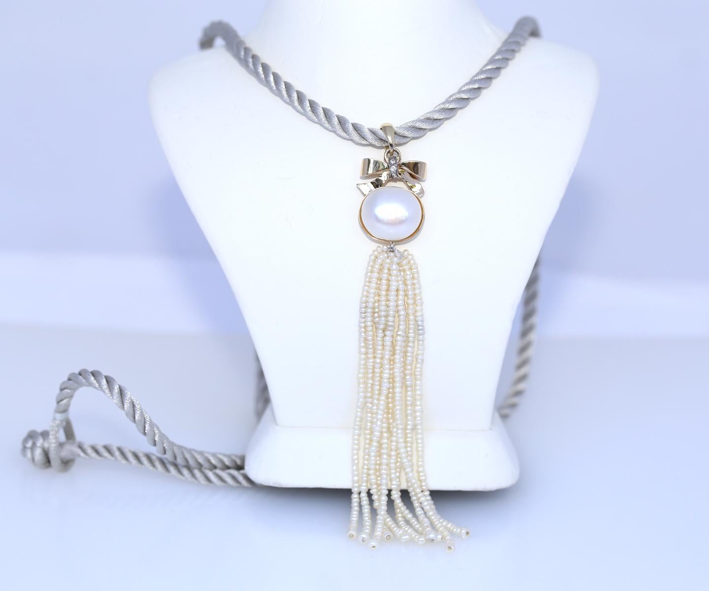 Modern design, pendant depicting a Gold bow with tiny Diamonds that holds a Pearl and multiple rows of tiny pearl beads. A simple, yet stylish grey cord is holding the pendant. 
The pendant moves in tune with the motion of the body.

Elegant item a
