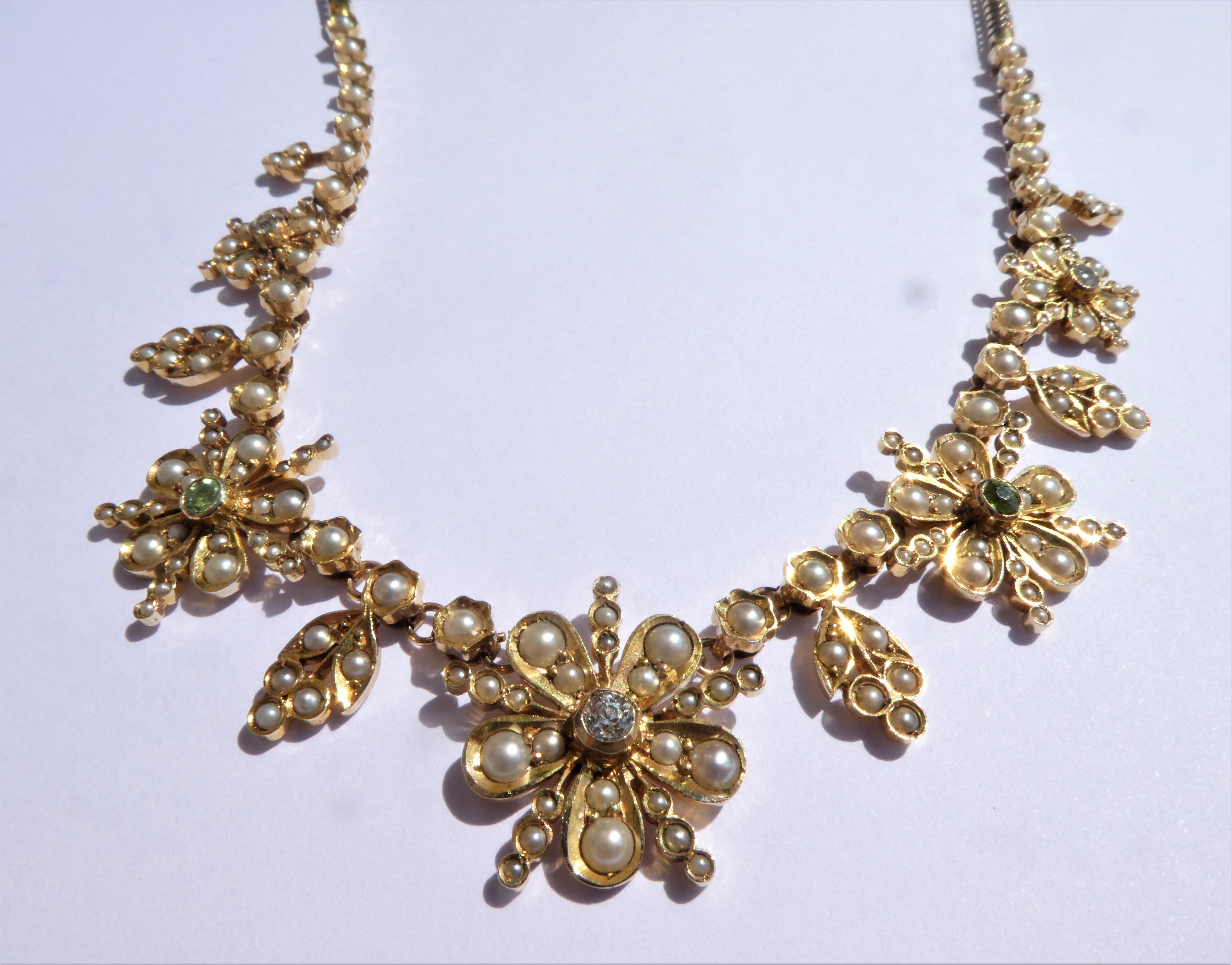 This diamond, peridot and half-pearl necklace is typical of the period around 1890 in England. It is designed as a row of five flowerheads connected by a chain with foliate motifs. The necklace was crafted in 14 karat yellow gold with white natural