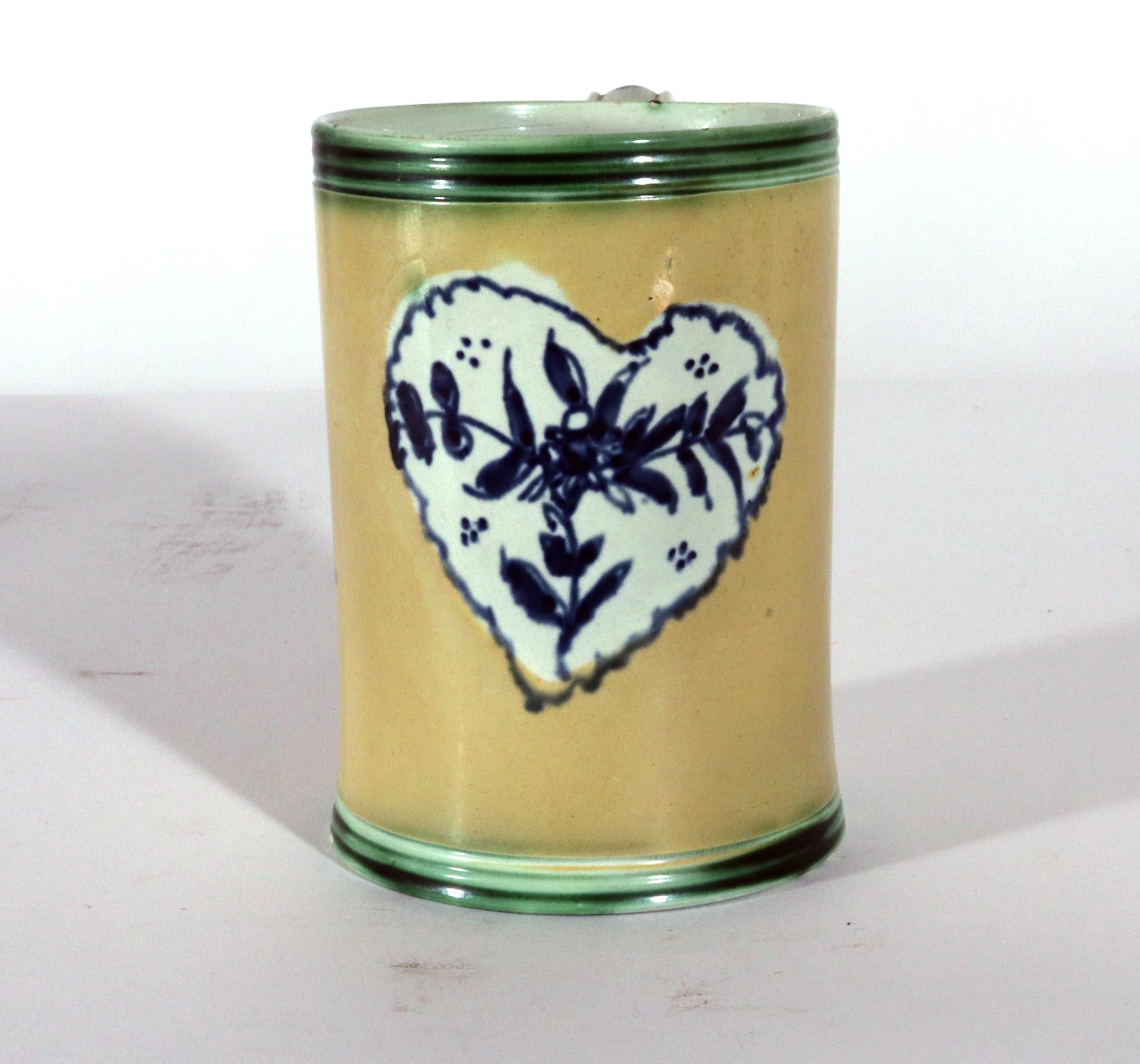 Mug en porcelaine avec fond jaune et décoration en forme de coeur,
Circa 1780

Cette chope ou tasse à fond jaune décorée à l'engobe est exceptionnellement peinte d'un panneau en forme de cœur avec une peinture en bleu sous glaçure d'une plante en