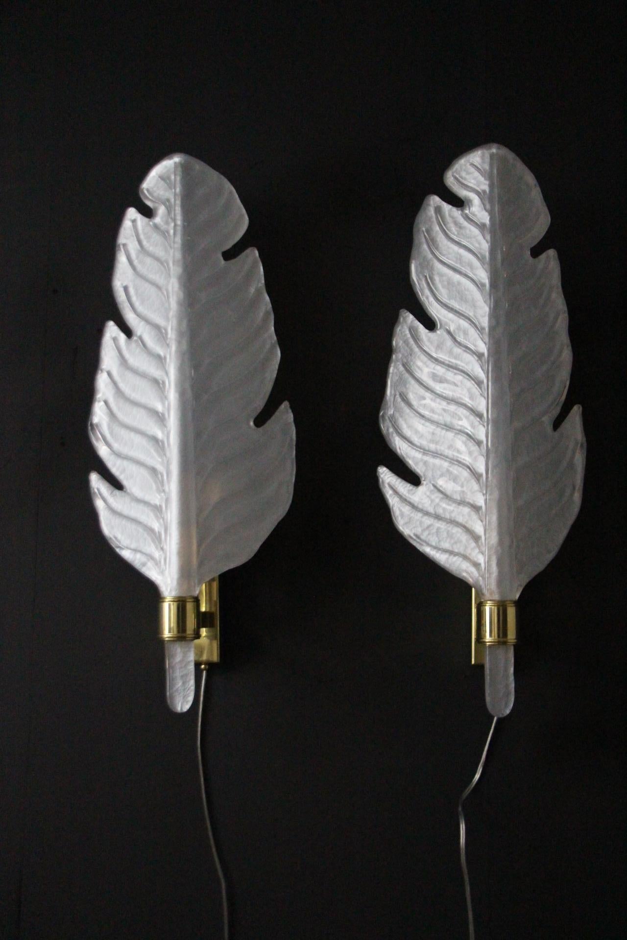 This is a very nice pair of pearly milk white blown Murano glass sconces in a shape of a leaf or a feather on a polished golden brass structure. Its curvy shape is very pleasant  and realistic as we can see the detailed leaf veins. They've been