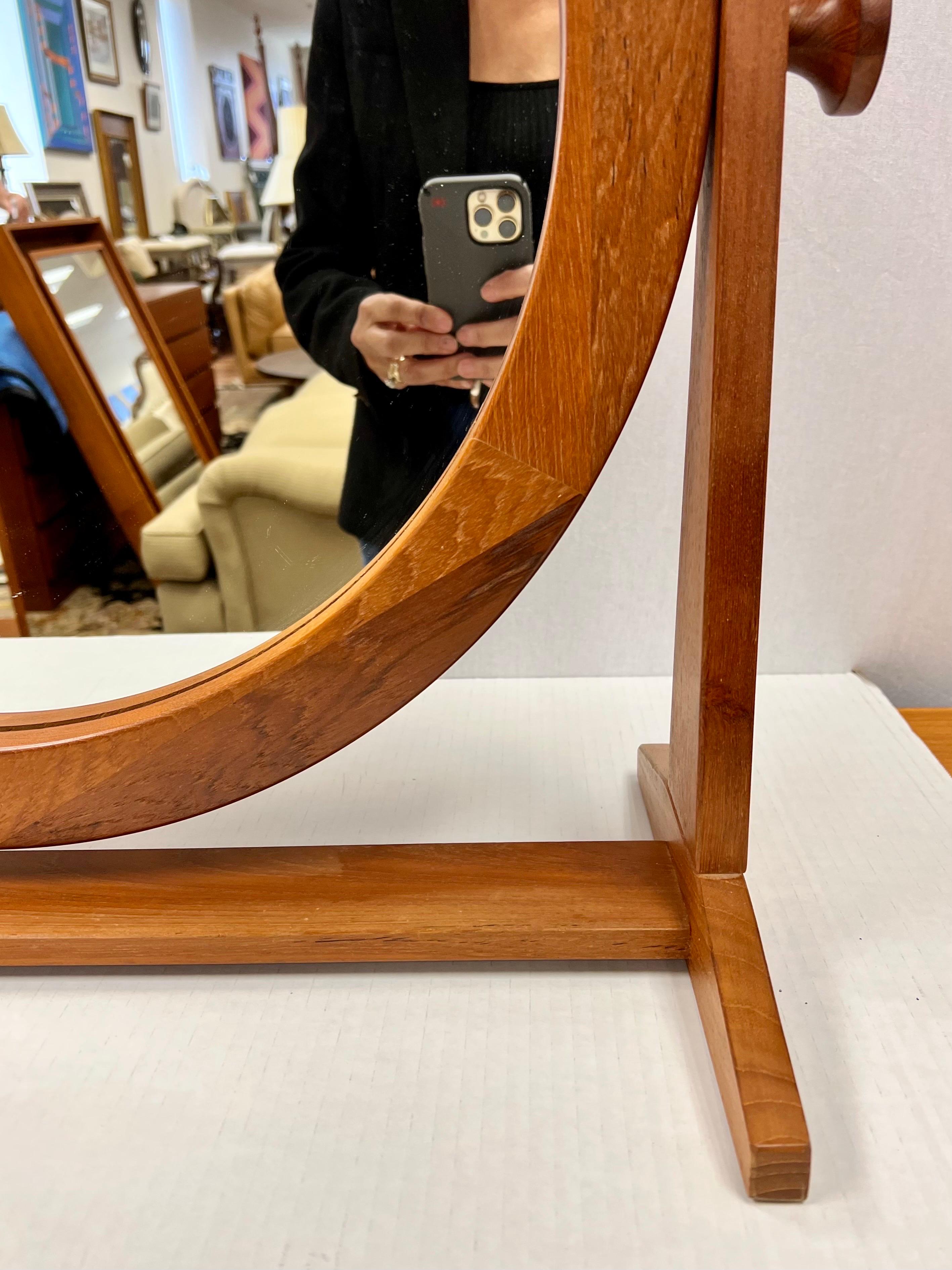 Danish modern vanity cheval mirror by Pedersen & Hansen. The glass portion is 19.5 inches in diameter and the frame with the knobs is 28 inches wide. The frame is made of teak. The mirror frame has great finger joint details. The mirror can tilt up