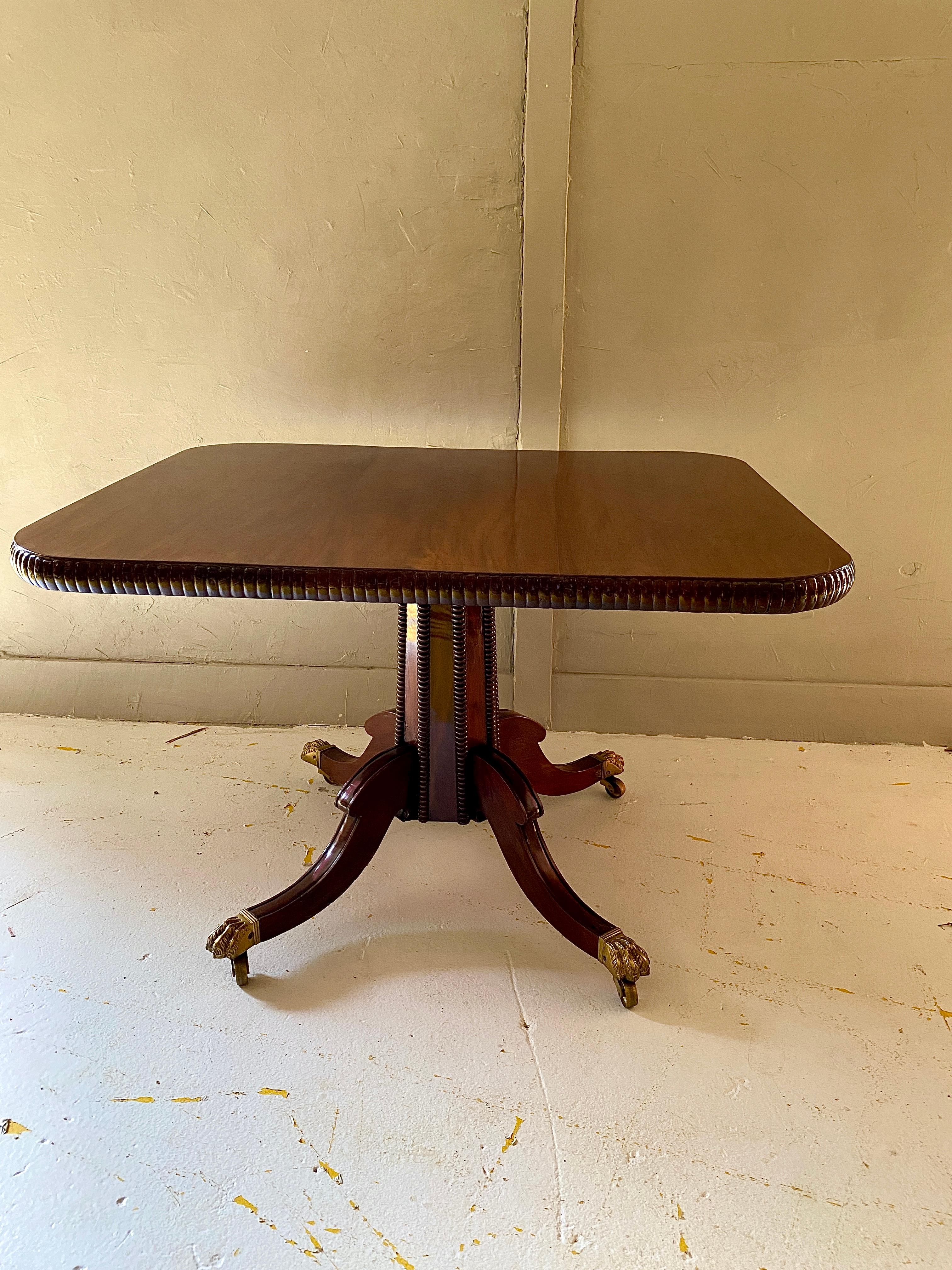A Stunning rectangle center table from the late 1800s. This beautiful mahogany table features a high glossy finish and a pedestal base with Brass Claw foot on caster wheels. The table top showcases Gadrooning Banding around the table top and Legs.