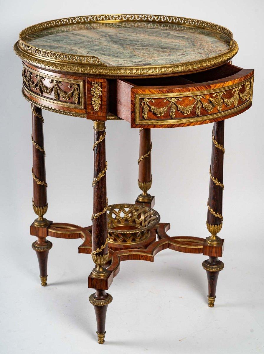 A round mahogany and violet wood veneer pedestal table, decorated with chased and gilt bronze, the top in fluorspar marble, with an ormolu gallery, resting on four tapered legs joined by an interlaced brace topped by an openwork bronze basket and