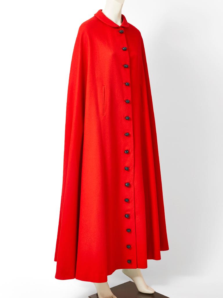 Pedro Rodriquez, red wool, maxi cape, having a small round collar , slits for the arms and black sculpted button closures going down the middle front of the cape.