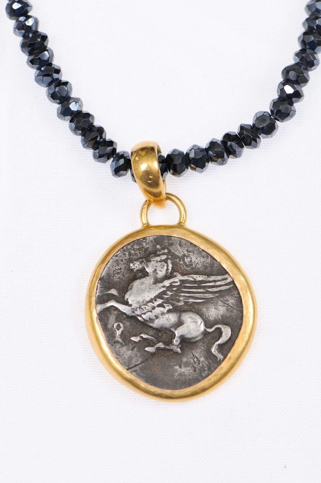 Ciondolo a forma di statere in argento, coniato ad Akarnia, nell'Antica Grecia, intorno al 350-320 a.C.. Sul dritto c'è la testa di Atena, sul rovescio Pegaso che si slancia verso sinistra. Questa moneta è stata ispezionata e approvata come