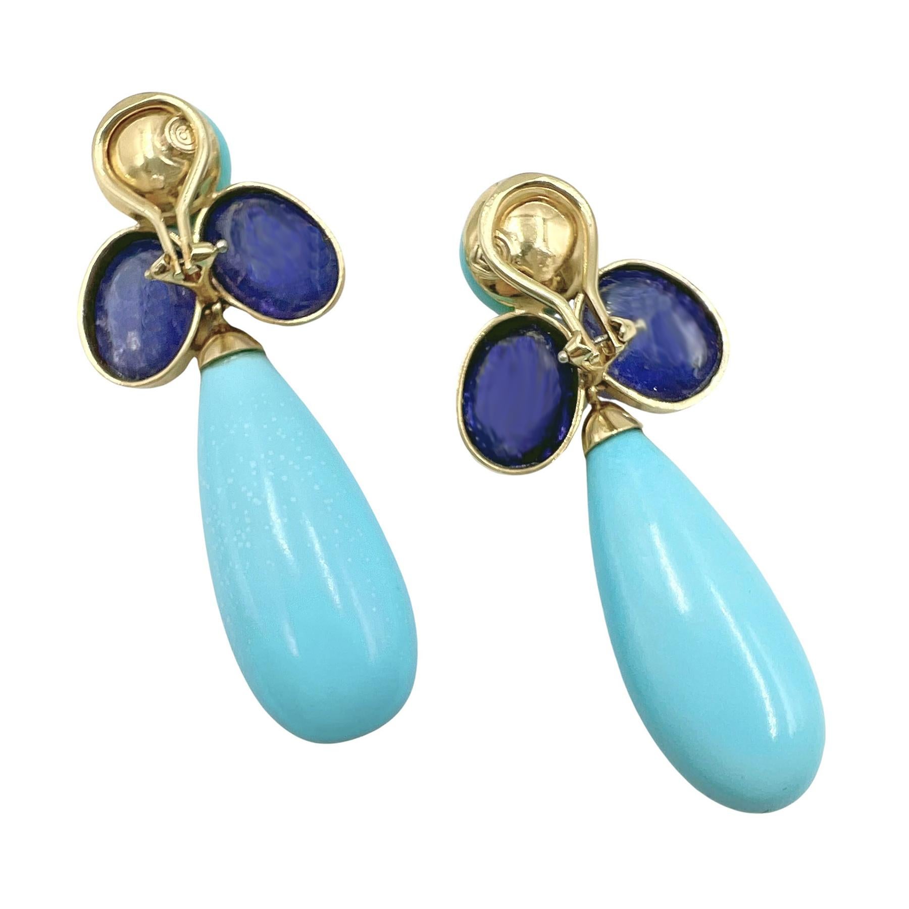 Pendientes Peggy Stephaich Guinness de oro amarillo de 18 quilates, cada uno con una turquesa en forma de lágrima suspendida de un racimo de dos tanzanitas ovaladas talla cabujón con una turquesa circular talla cabujón en la parte superior.  Cada