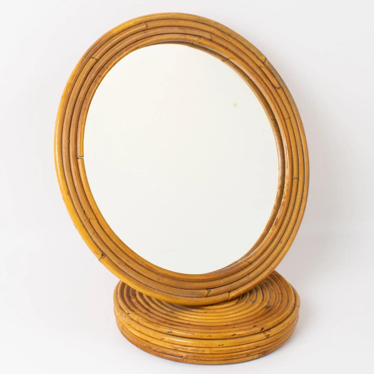 This lovely rattan or bamboo Italian table mirror from the 1960s features a rounded frame built with pencil reed wicker and a mirrored glass insert. There is no visible maker's mark. 
The mirror is in good condition, with minor wear on the mirrored