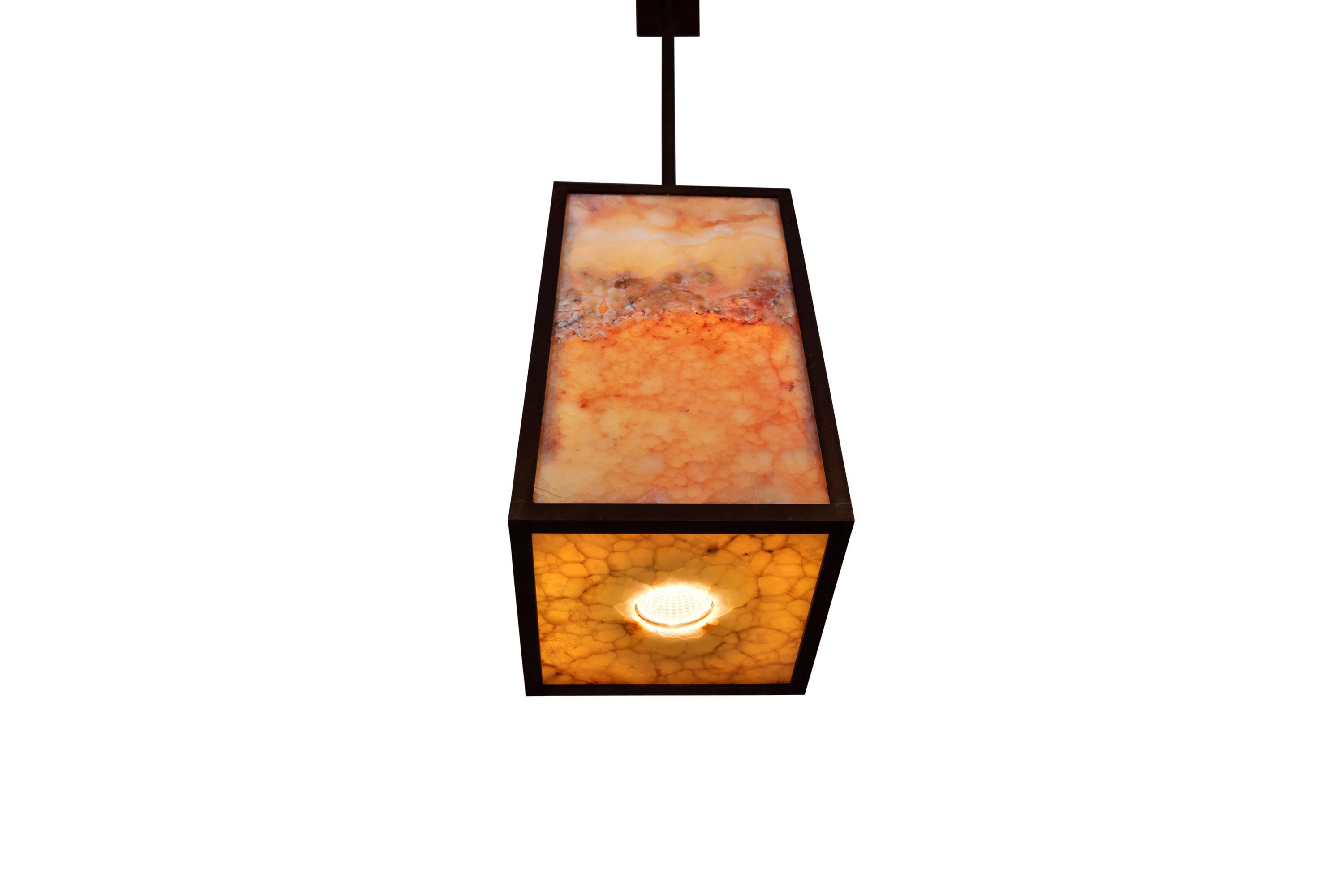 Pendant made of blackened brass profiles with onyx marble sheets which are translucent, filled with leds and below a hole with a MR16 spot light led. Power supply on distance. Overall height is 76 cm but can be adapted.