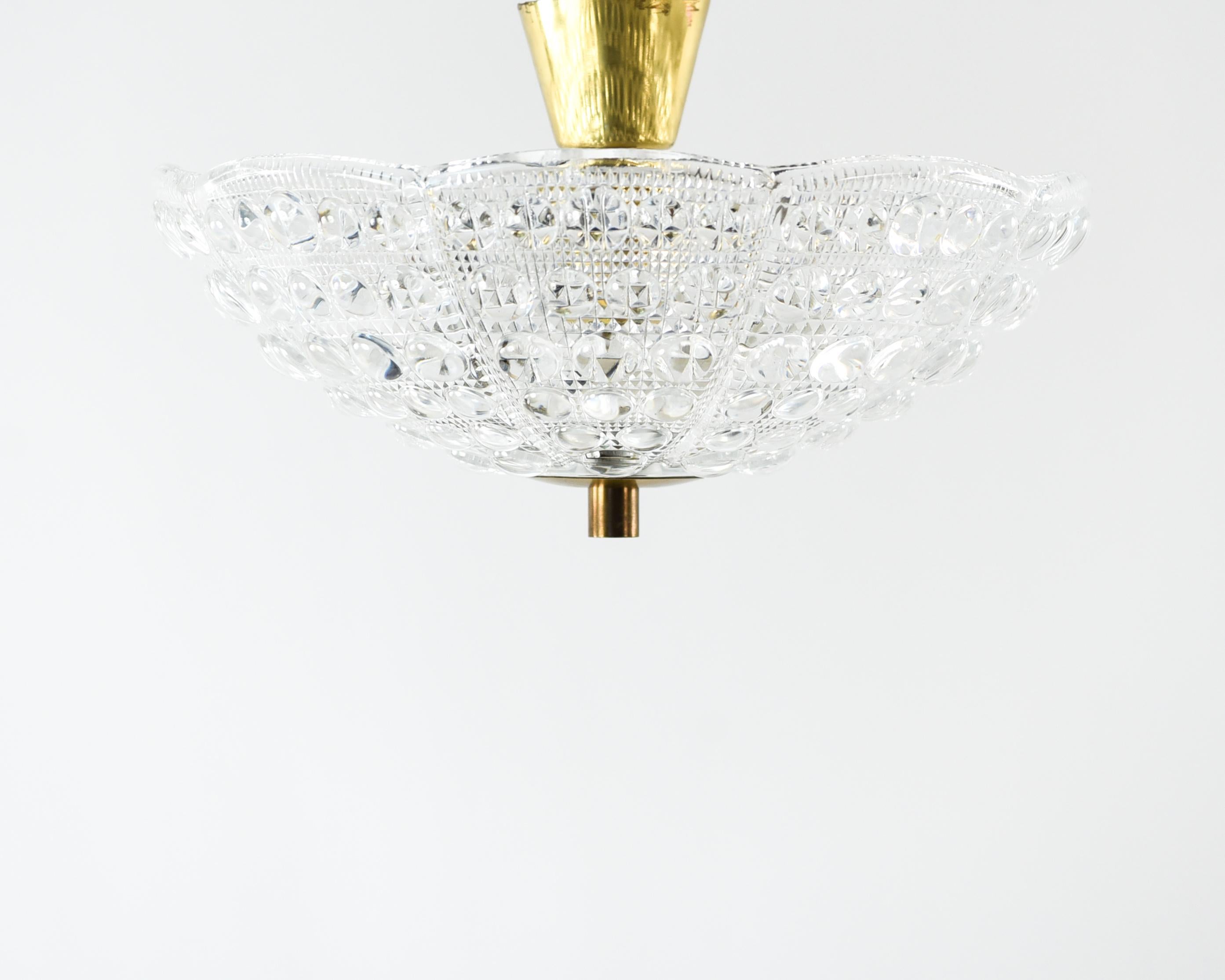 This pendant chandelier was designed by Carl Fagerlund and produced by Orrefors, circa 1960s. This elegant piece features textured crystal in a rounded, shallow conical form with brass hardware and accents.