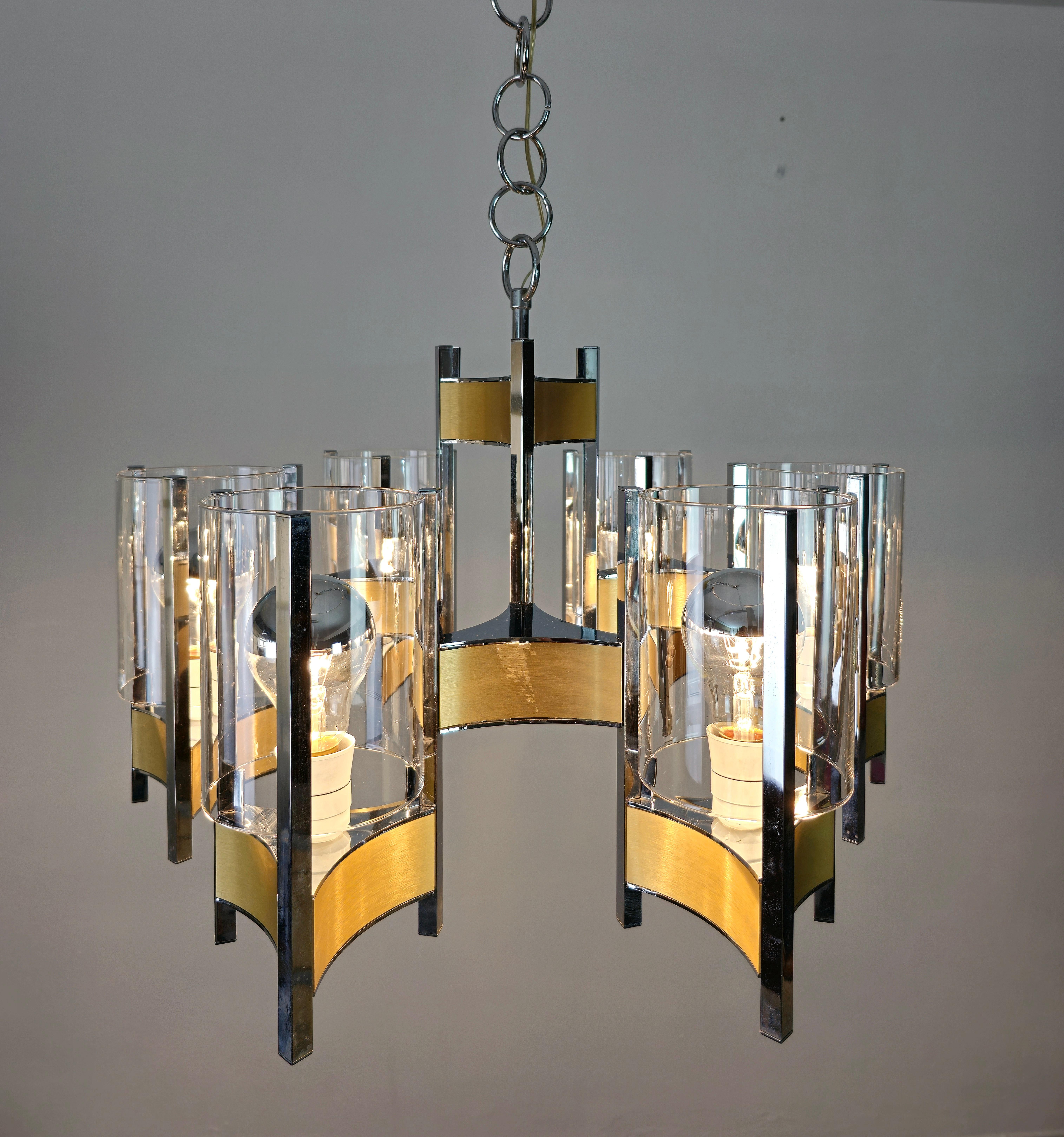 Elegant chandelier by Gaetano Sciolari with 6 E27 lights made with stems in chromed nickel finish and brushed brass colored panels, where each arm supports a transparent cylindrical glass. Made in Italy in the 60s. It has the original Sciolari stamp