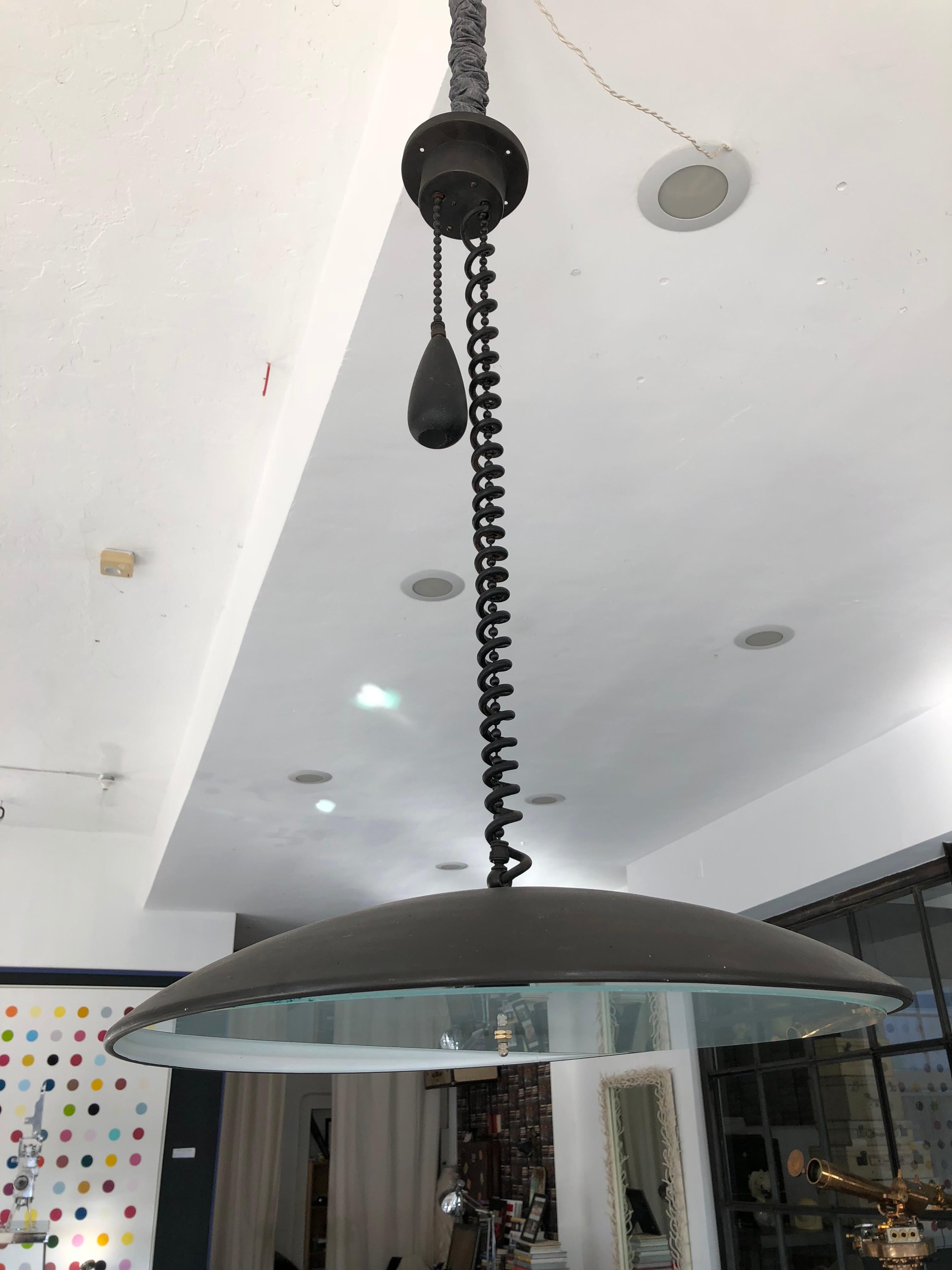 Lampe pendante industrielle à contrepoids d'après Paavo Tynell, années 1940. Laiton massif recouvert d'une patine noire. Le pendentif mesure 24 pouces de diamètre et 5 pouces de hauteur.