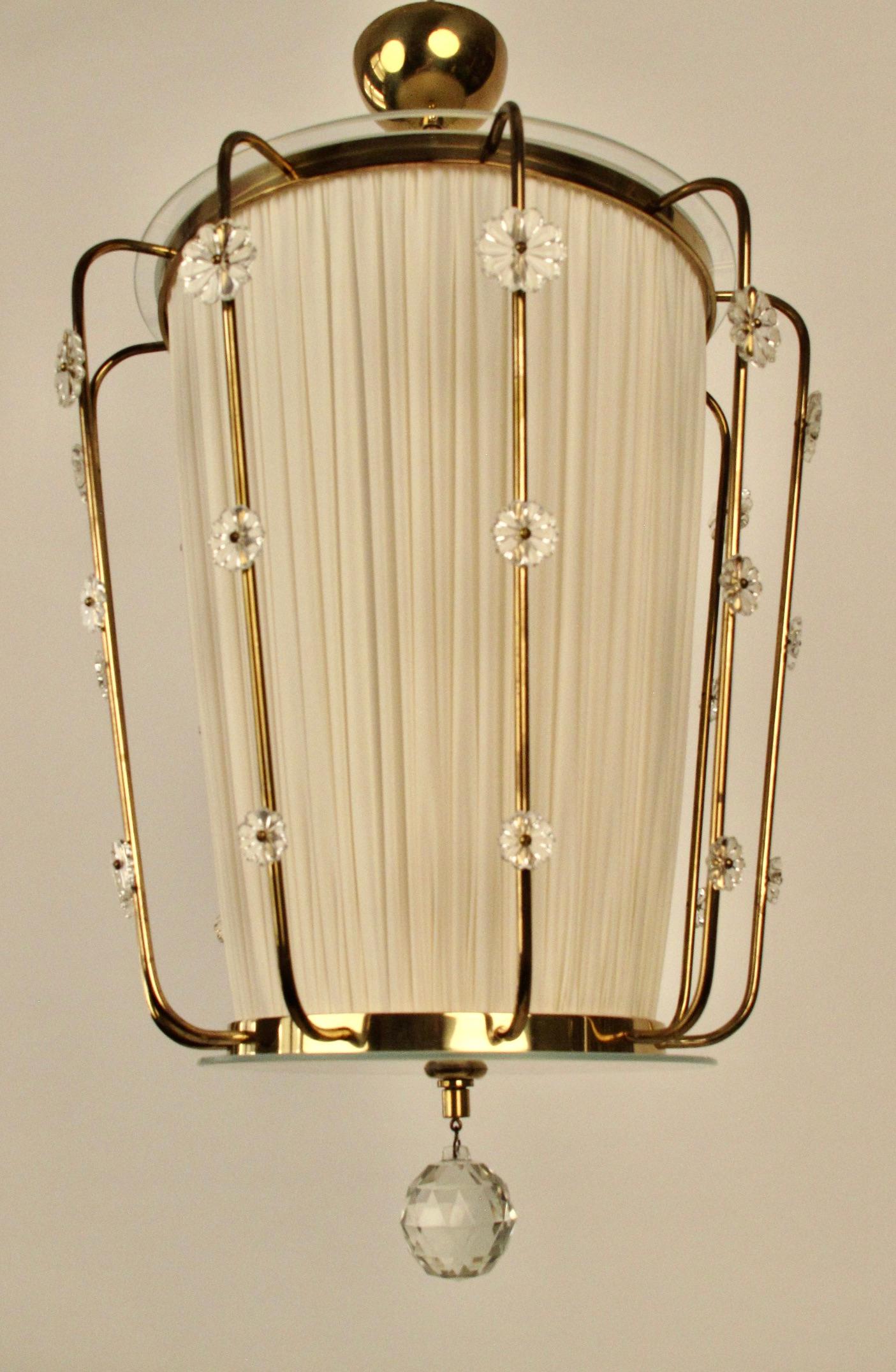 This pendant lamp was made by J. L. Lobmeyr in he 1950's.
 It is composed of a brass frame with a silk shade and two round glass plates, one on the top and one on the bottom. The metal work is all done by hand, as one can see from the photographs