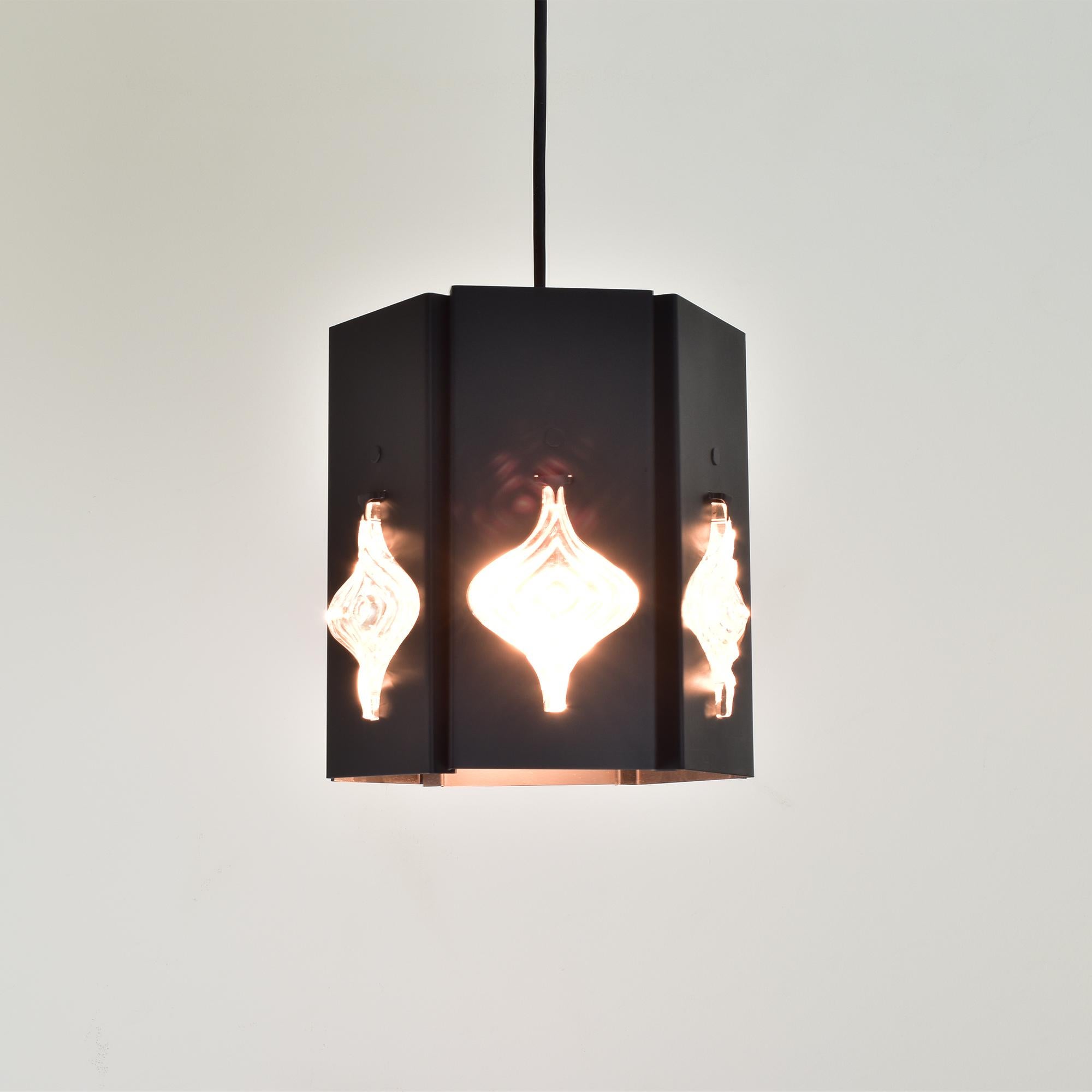 Questa suggestiva lampada a sospensione, frutto della collaborazione tra Erik Höglund e Einar Bäckström, svedesi, negli anni '60, mostra un mix di estetica modernista e artigianato scandinavo. La lampada presenta una struttura geometrica in metallo