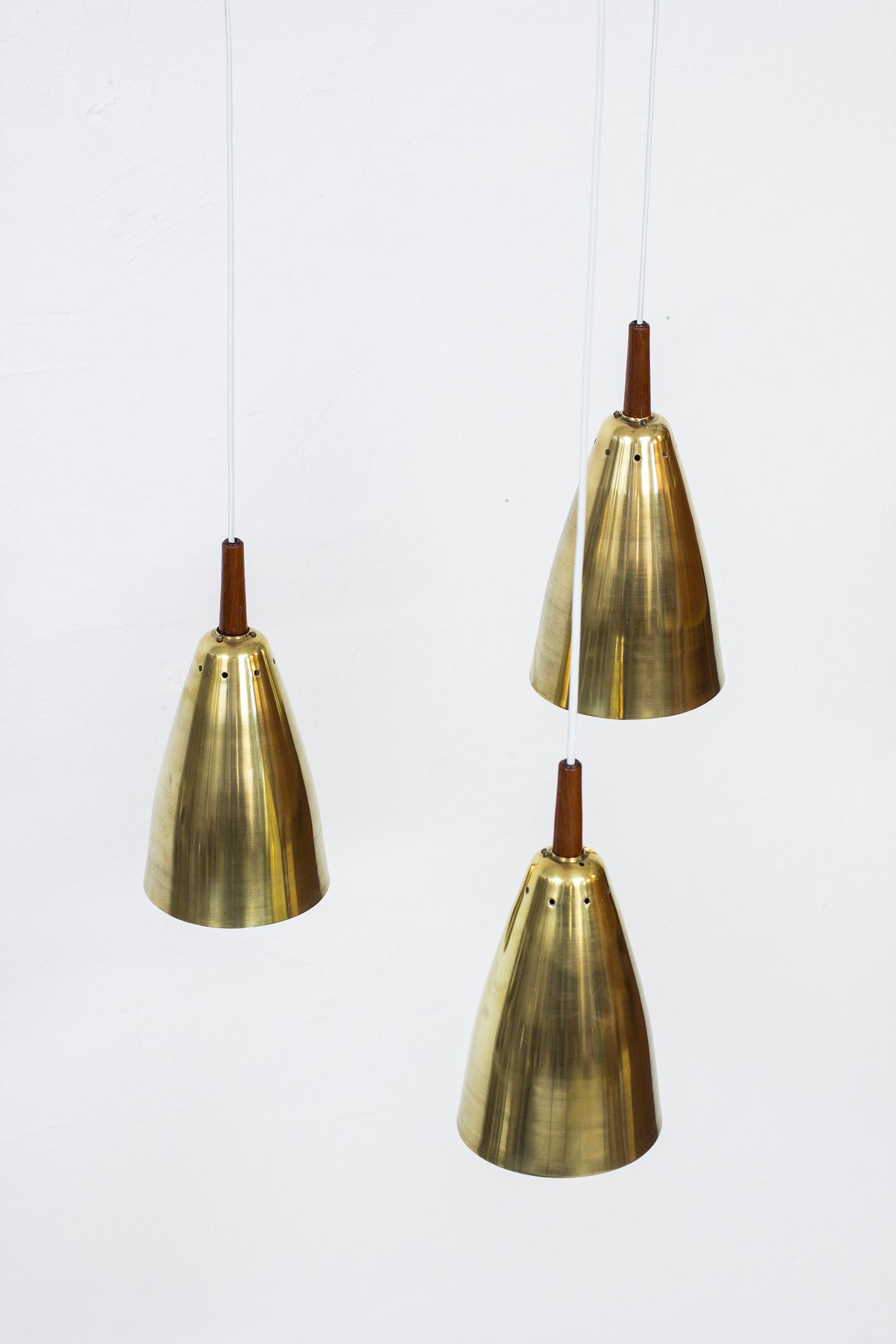 Tripple pendant lamp designed by Hans-Agne Jakobsson. Produced by his own company in Åhus during the 1950s. Three solid brass shades and ceiling mount with teak details and solid teak triangle that separate the shades. Signed with label. Very good