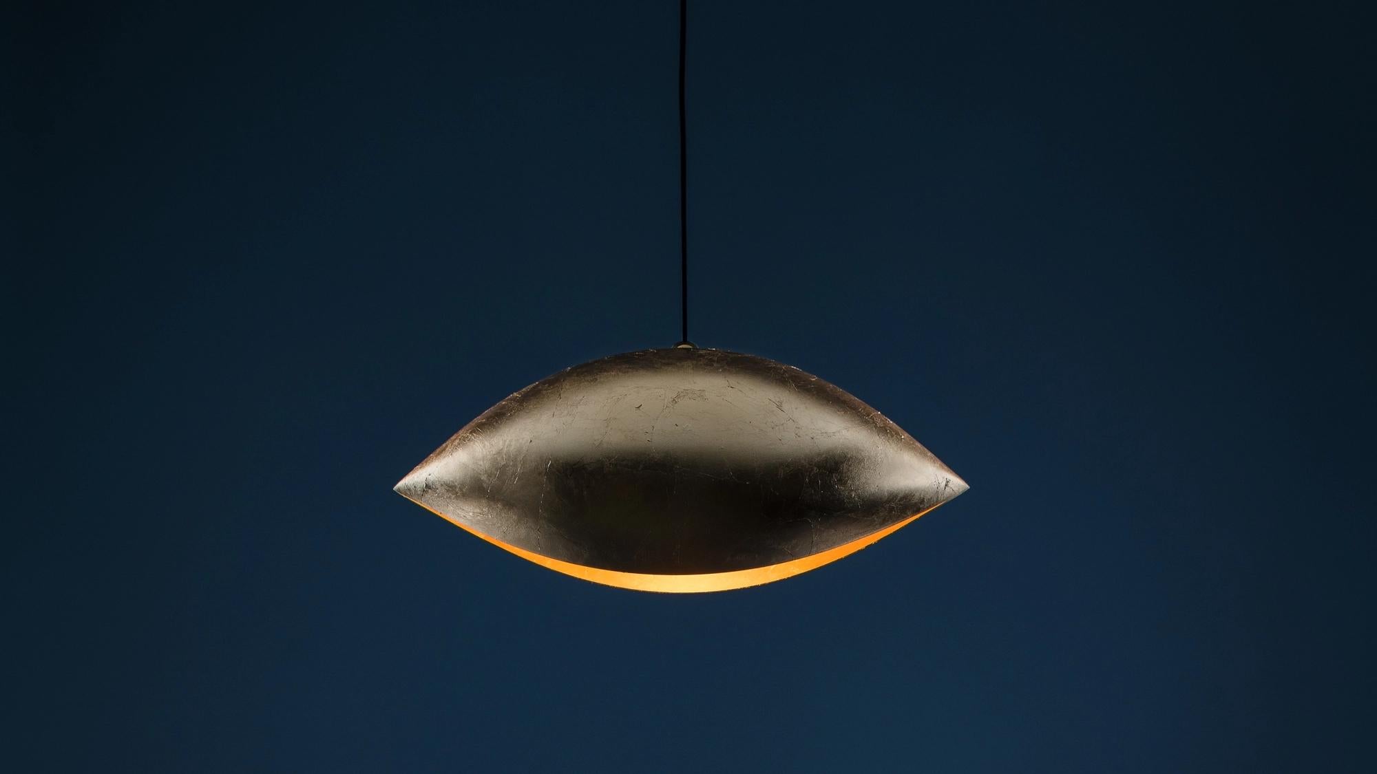 La Malagola 55, parte della collezione Luci d'Oro di Enzo Catellani, è una lampada a sospensione che esplora il calore dorato della luce ispirandosi al sole e al fuoco. Il suo design cattura il gioco poetico della rifrazione e dei riflessi luminosi,