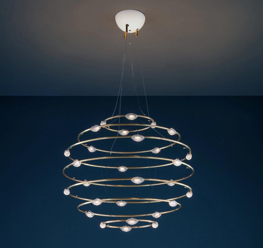 Il Petits Bijoux, disegnato da Enzo Catellani, cattura l'essenza di un movimento statico: l'increspatura congelata di una pietra lasciata cadere nell'acqua, che forma onde concentriche che si irradiano nello spazio. Questa lampada a sospensione