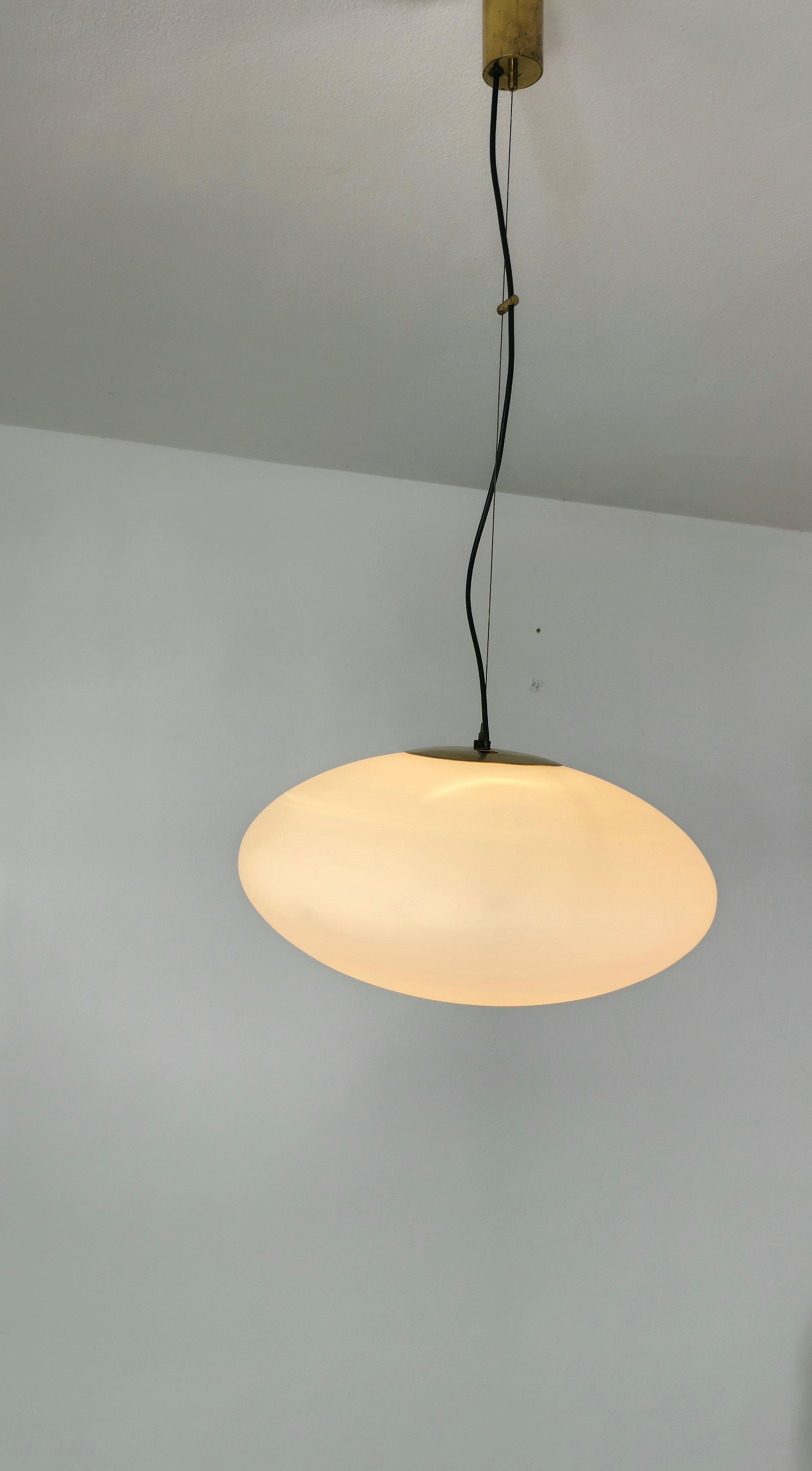 Stilnovo model 1104 suspension lamp has an ellipsoid-shaped opal glass diffuser. The glass is supported by a brass accessory which allows the glass to change its slope or balance according to one's taste. All supported by a steel wire with a brass