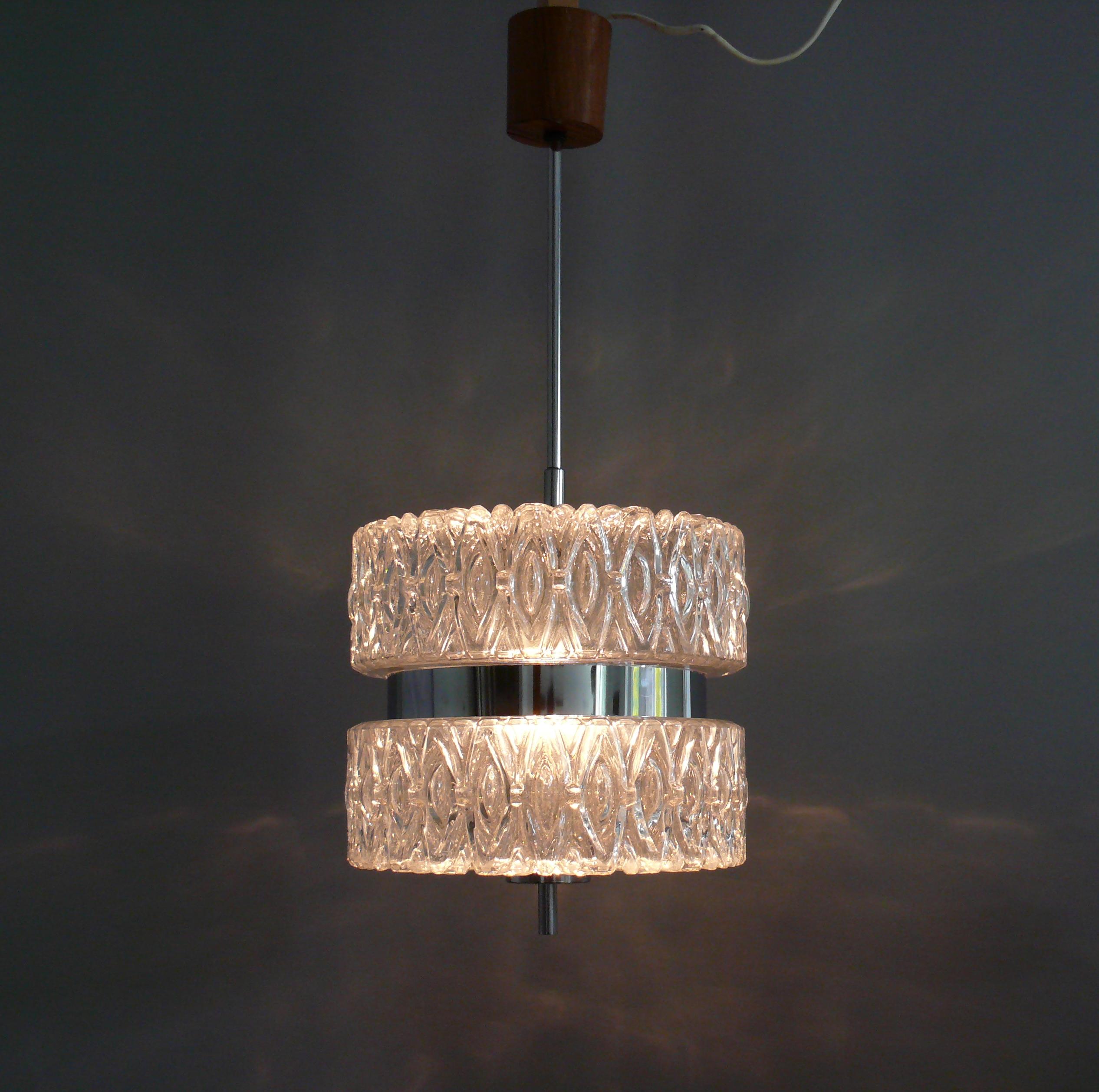 Crystal glass pendant lamp from the late 1960s - early 1970s. The two solid glass shades are interrupted by a chrome strip and held together inside by a metal bracket. The chrome pendulum rod is screwed on and can be easily replaced. The canopy is