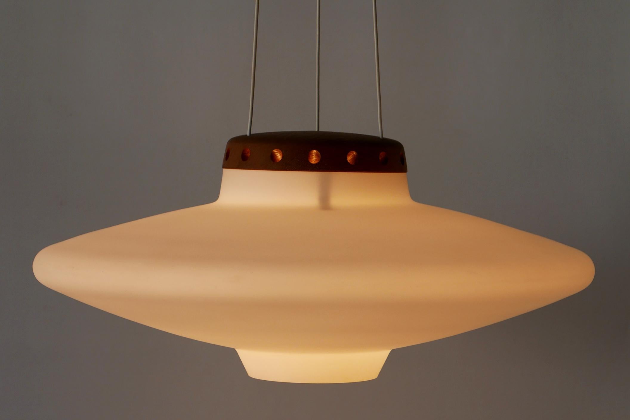 Elegant Mid-Century Modern pendant lamp or hanging light model 565 / UFO. Designed by Uno & Östen Kristiansson, 1950s for Luxus, Vittsjö, Sweden. 

Executed in matte opal glass diffusor and wood cover, the lamp comes with 1 x 27 / E26 Edison screw