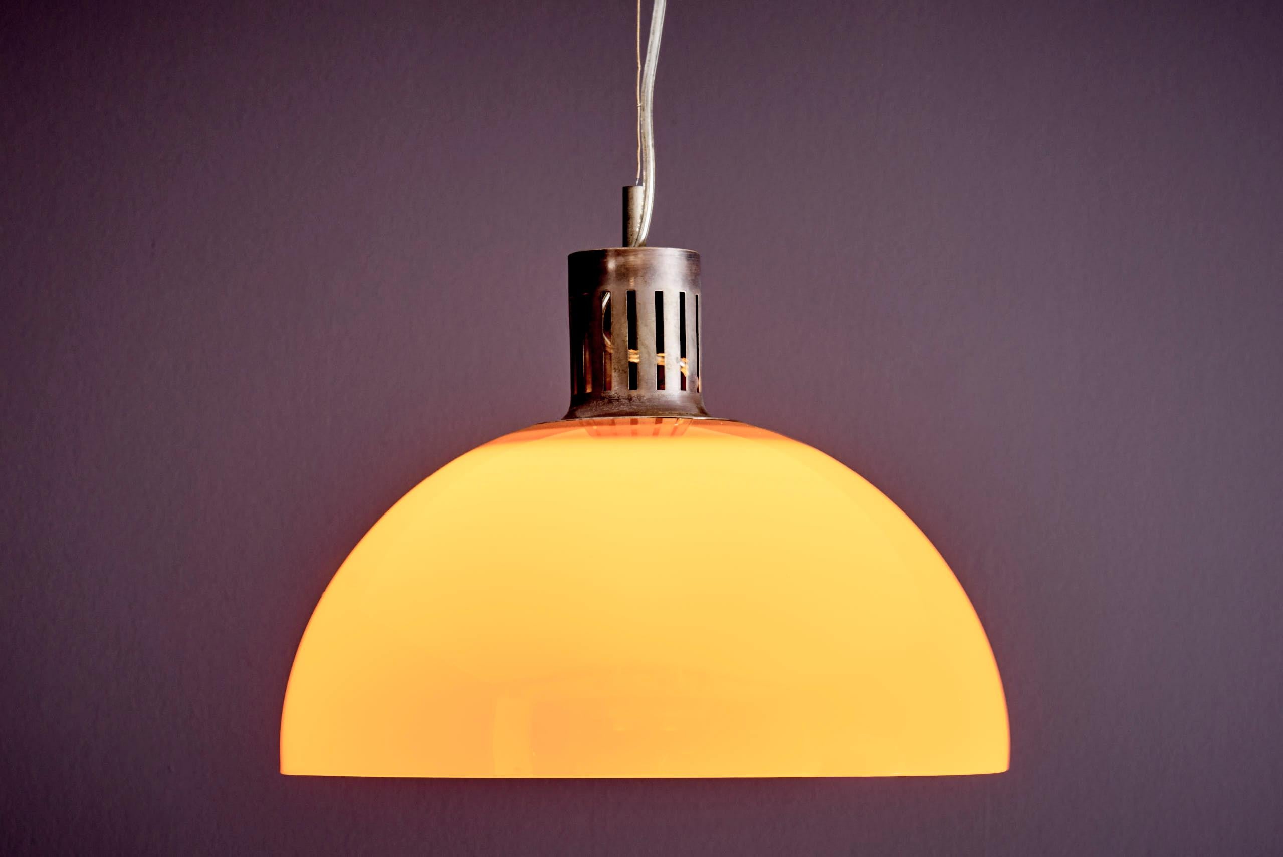 Questa lampada a sospensione italiana presenta un paralume a forma di cupola arancione brillante in acrilico, abbinato a un attacco in metallo perforato con finitura scura e patinata. L'altezza totale della lampada, compresa la sospensione, è di 88