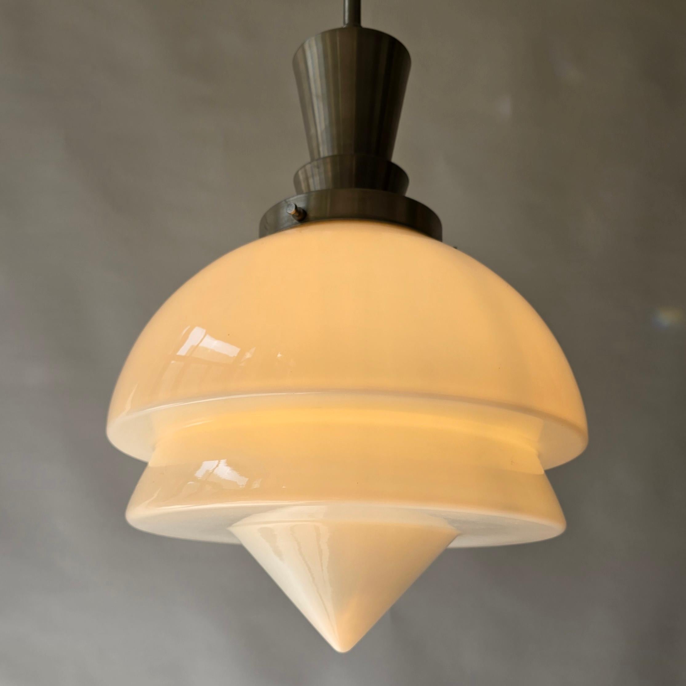 Lampada a sospensione progettata da Gispen, un rinomato produttore olandese famoso per i suoi design industriali senza tempo. 

Questo elegante apparecchio è caratterizzato da un paralume in vetro opalino di ottima fattura con una forma geometrica