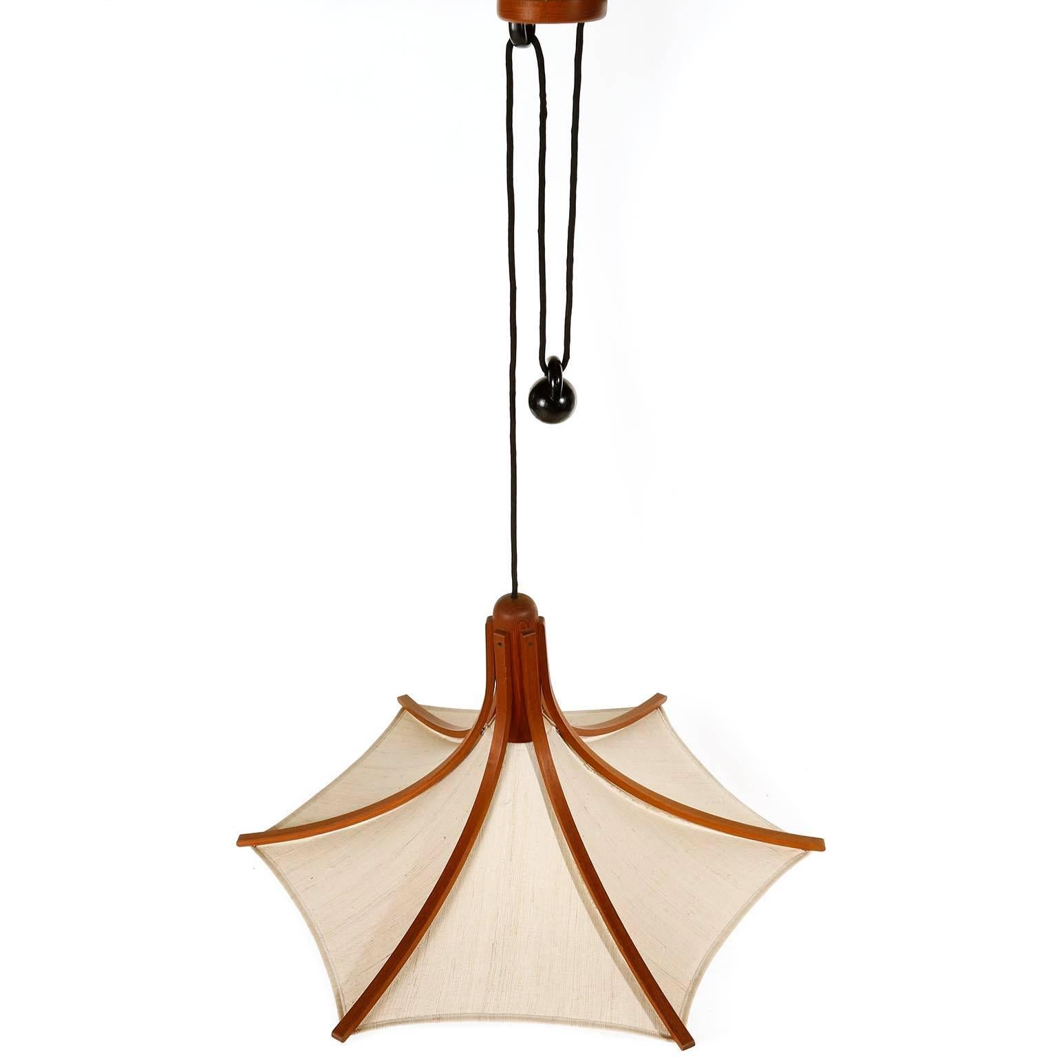 A large height adjustable counter balance pendant light manufactured in Denmark in midcentury, circa 1960 (late 1950s or early 1960s).
This Danish modern design lamp is made of a teak frame which is covered with linen. The drop can be adjusted with