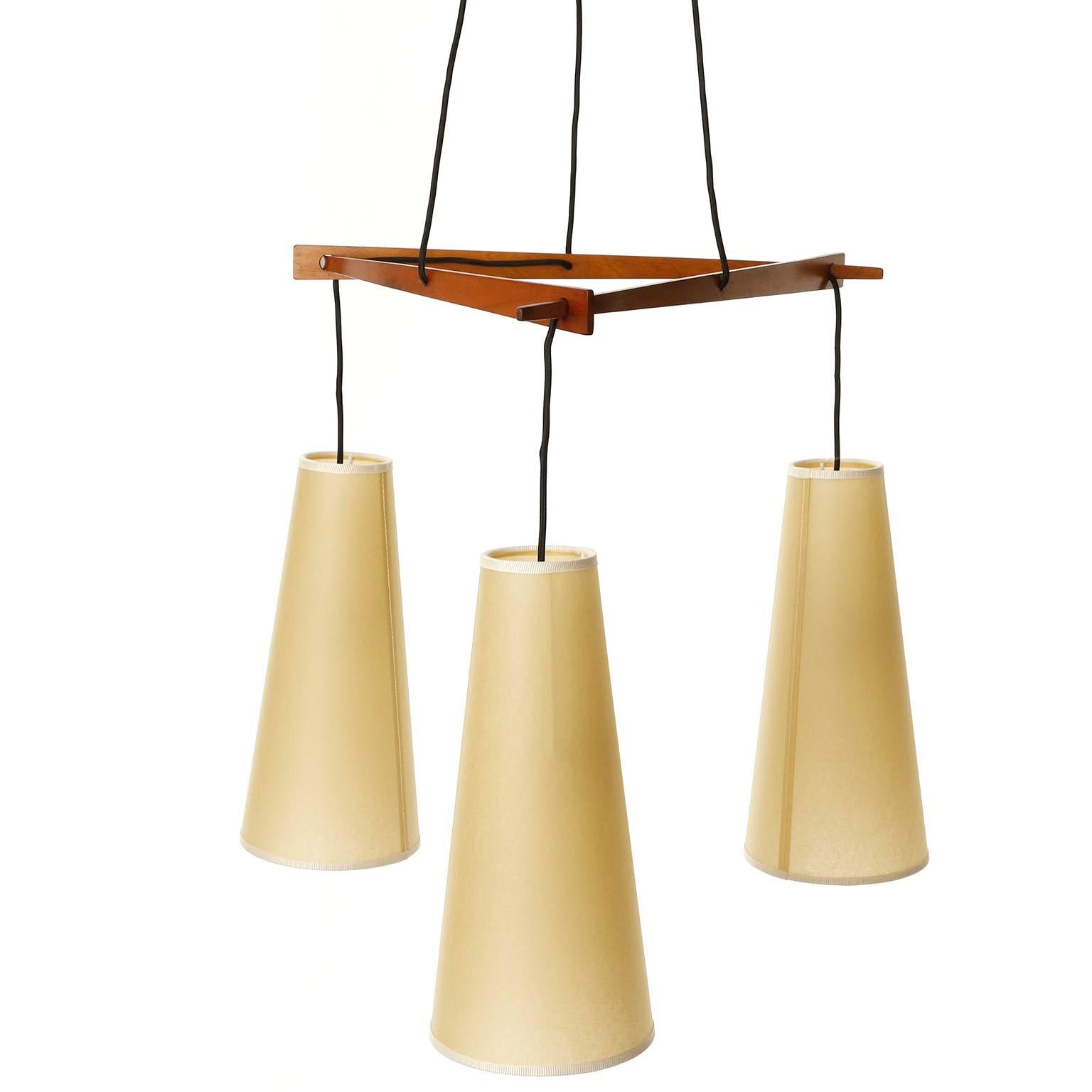 A fantastic pendant light model 'Dreistich' no. 3759 made of brass and walnut wood with parchment lamp shades by J.T. Kalmar, Vienna, Austria, manufactured in midcentury, ca. 1960 (late 1950s or early 1960s).
The wooden parts are in very good