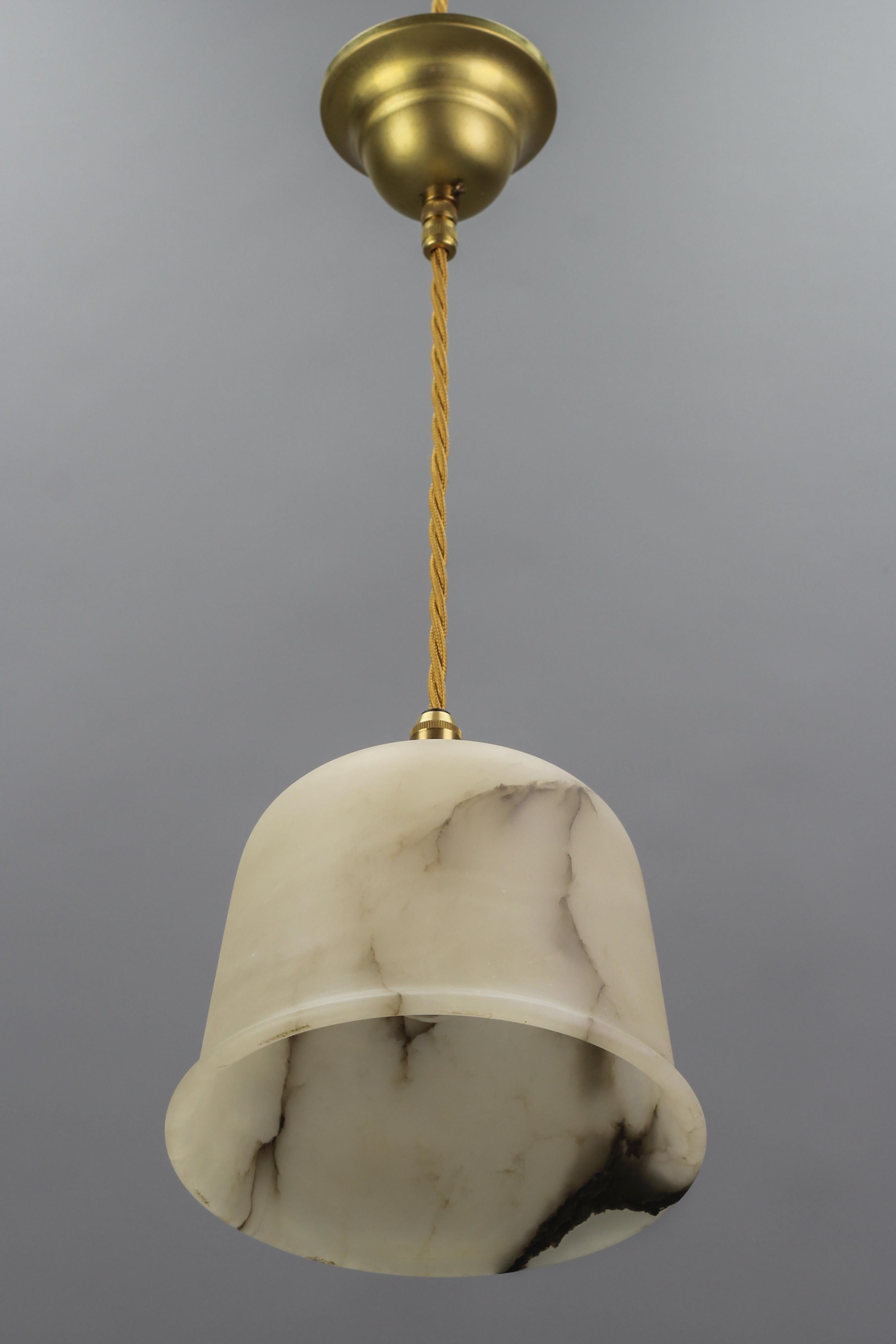 Adorable and compact Art Deco alabaster pendant light.
The beautifully veined white and black alabaster lampshade is suspended from a brass canopy. The light shining through the white stone with dark brown and black veins is warm and atmospheric,