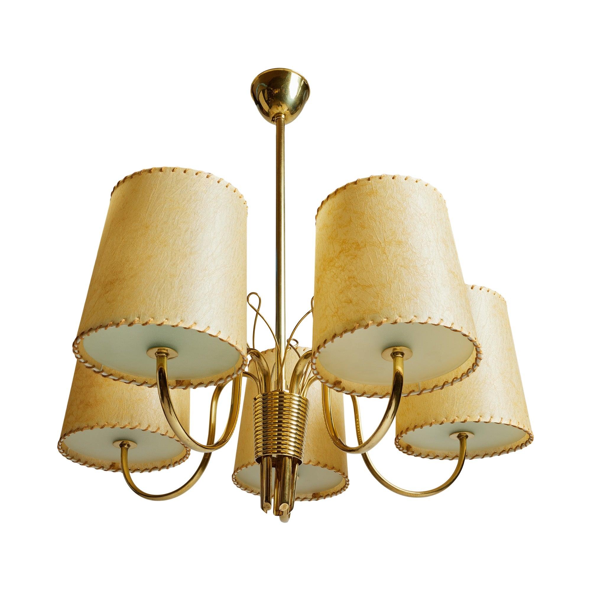 Lampe suspendue en laiton poli, dotée de cinq bras gracieusement courbés émergeant d'une coupelle nervurée à la base. Cinq fils de laiton, ressemblant à des pédales, partent du centre vers le haut. Chaque bras est muni d'un disque rond en verre