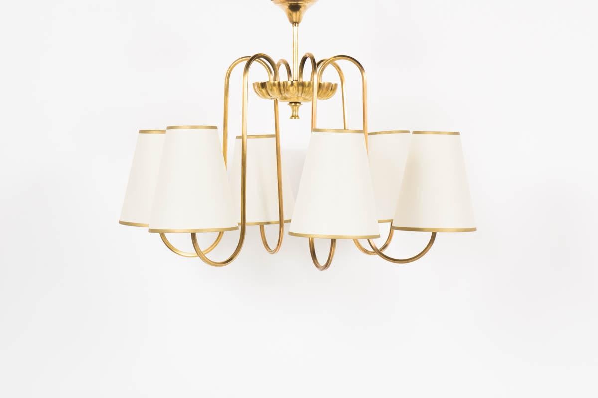 This elegant French pendant light was designed in the fifties. It consists of a solid brass central fixation which is attached 6 arms also in brass each finished by a beige paper lampshade and gold edges. 
The golden color edge was chosen to remind