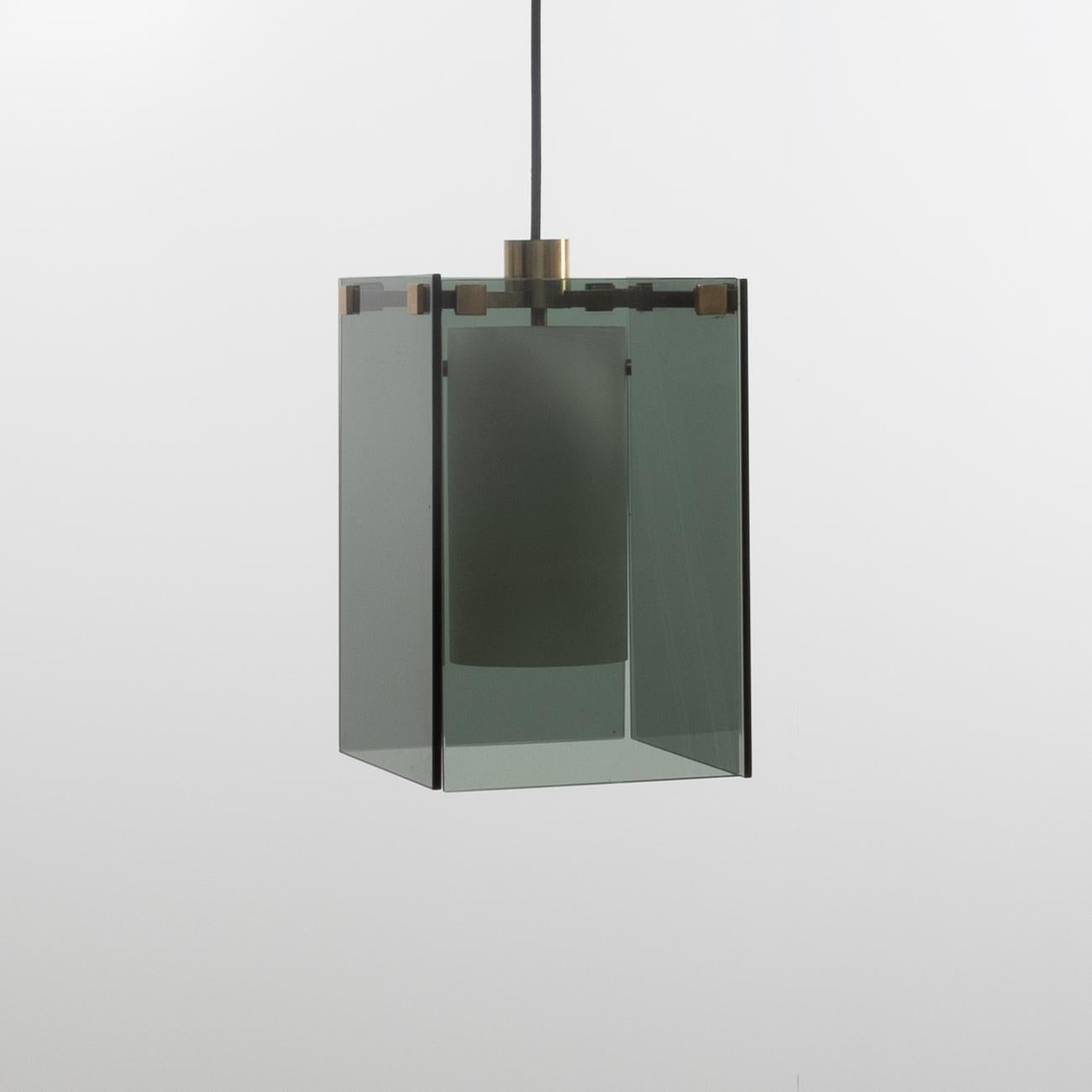 Hanging light made of four dark grey glass sheets held in place by an upper structure in the shape of a cross made of patinated brass. 
A white bulb cover hangs in the centre of the lamp to enable the light to be released in a subtle way. 
 
The