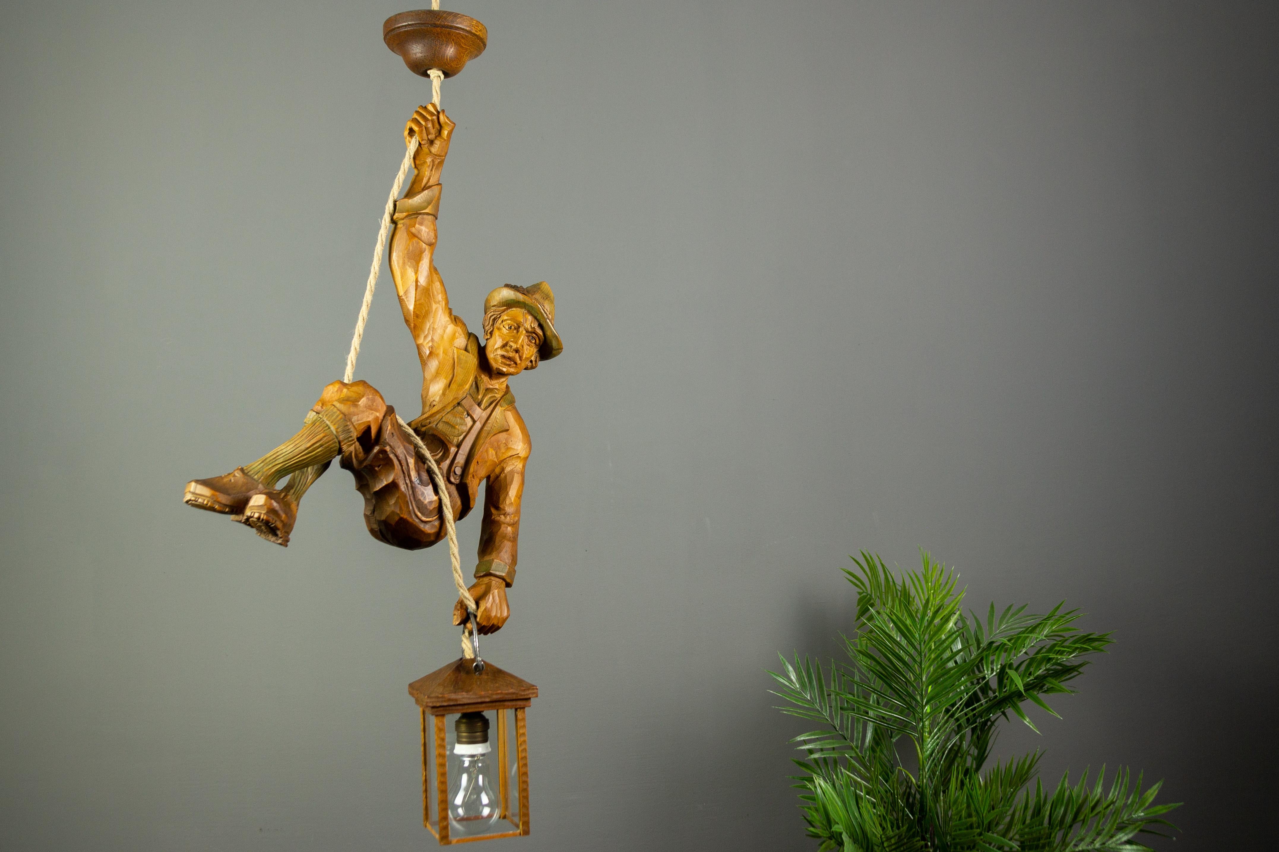 Merveilleuse lampe suspendue figurative allemande présentant une grande figure d'alpiniste sculptée à la main. L'alpiniste en bois sculpté se tient à une corde et tient une lanterne en bois dans une main. La figure est légèrement teintée de couleurs