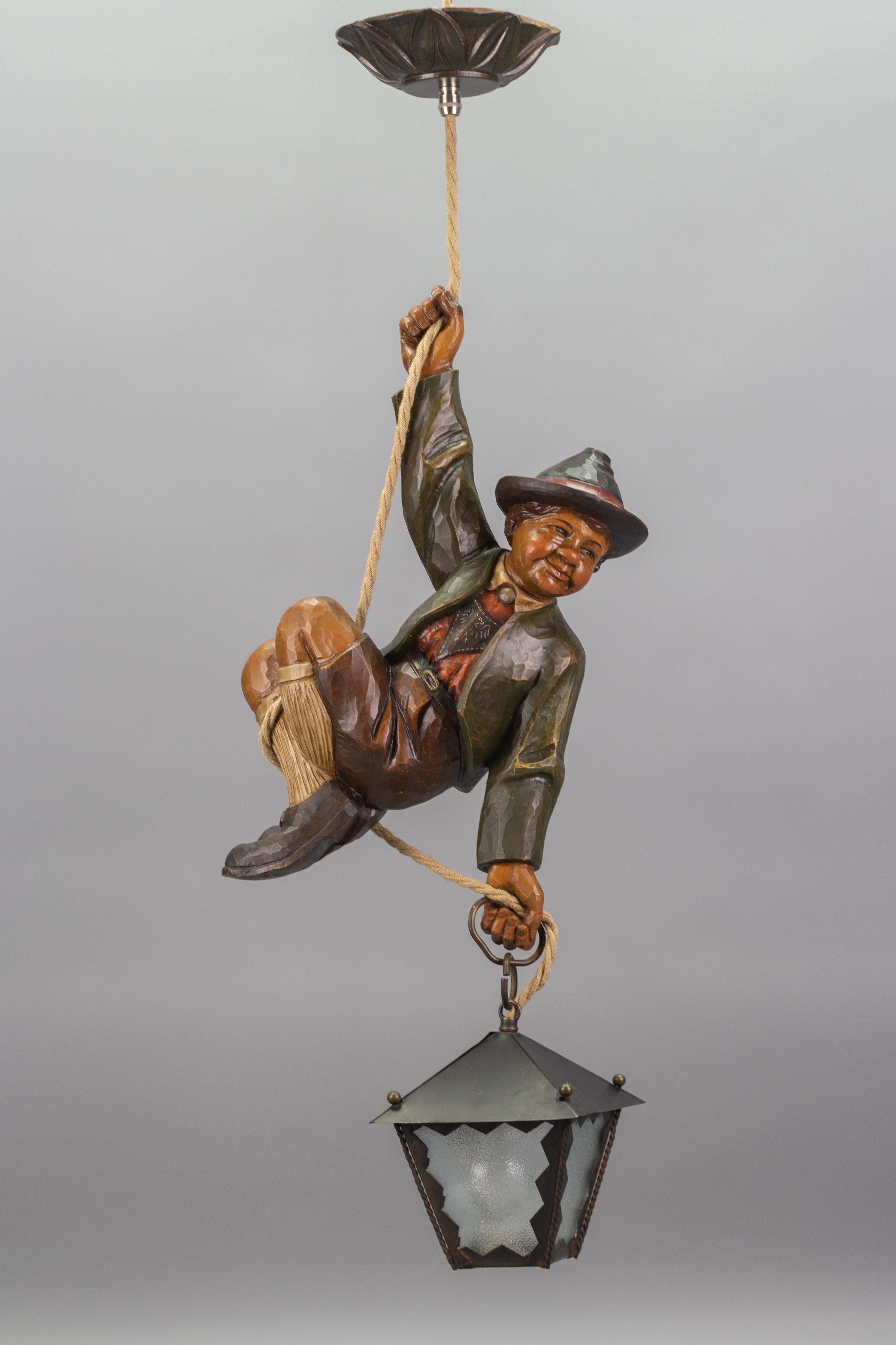 Wonderful German pendant lamp features a hand-carved figure of a smiling and cheerful mountain climber in beautifully hand-painted Bavarian traditional clothing in brown, green, white, and red colors. The detailed carved wooden figure wears a hat
