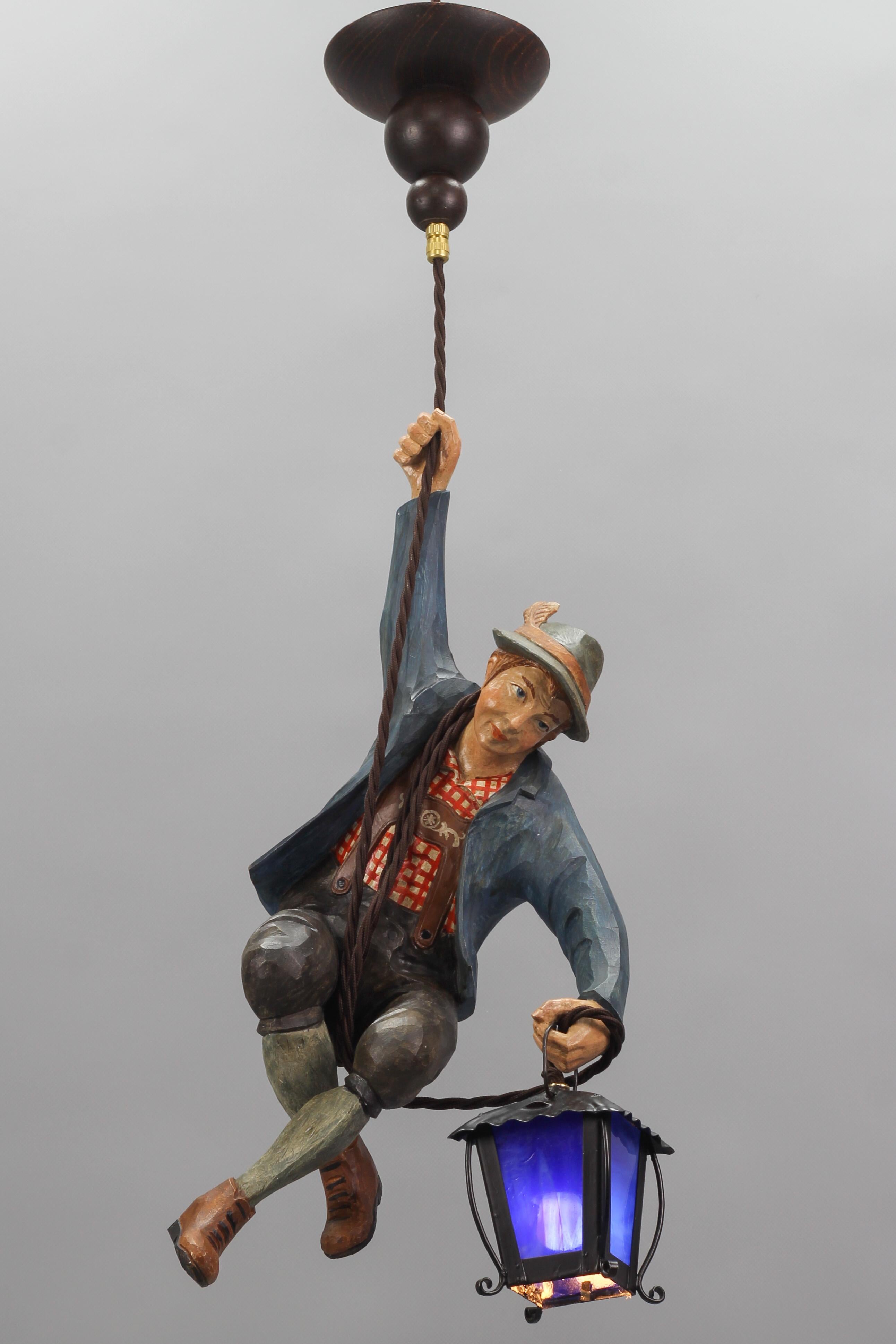 Wonderful German pendant lamp features a hand-carved figure of a smiling mountain climber in beautifully hand-painted Bavarian traditional clothing in blue, brown, green, white, and red colors. The detailed carved wooden figure wears a hat and is