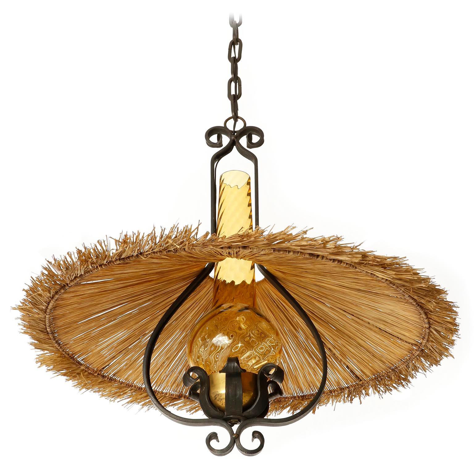 A pendant light manufactured in Austria in midcentury, circa 1960 (late 1950s or early 1960s).
It is made of nice mixture of materials and colors: blackened wrought iron, naturally aged and patinated brass, an amber colored glass and a lamp shade