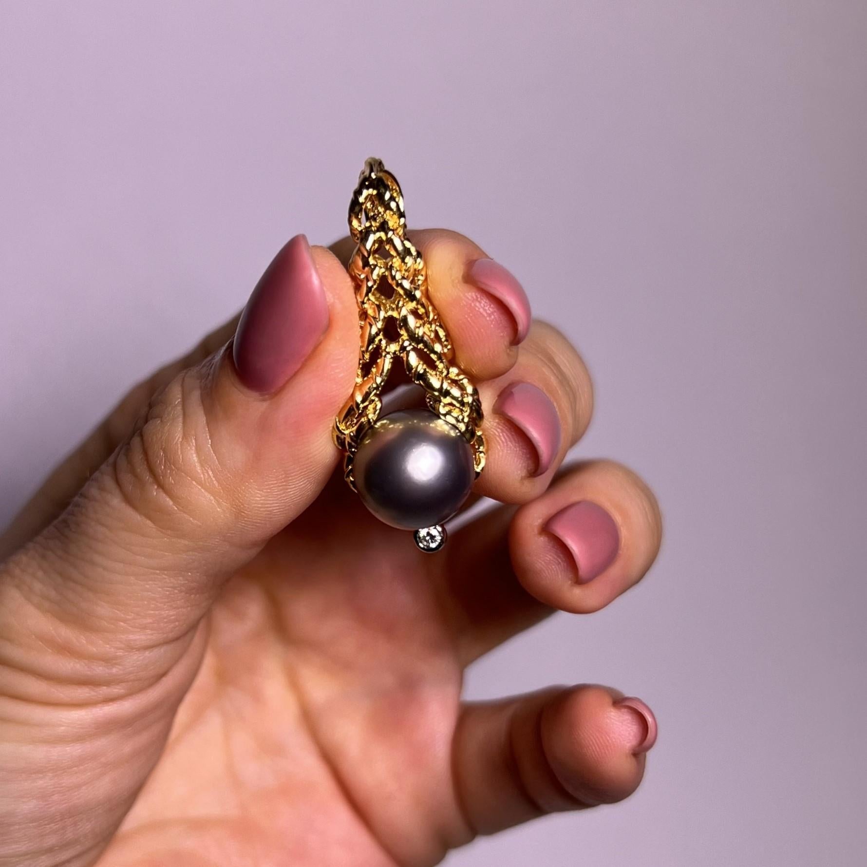 Découvrez l'attrait du pendentif exquis de Gilbert Albert : une étreinte tourbillonnante d'or jaune 18 carats entourant une perle de culture de Tahiti lustrée. Rehaussée d'un diamant taille brillant pesant 0,05 carat, de couleur G-H et de pureté VS,