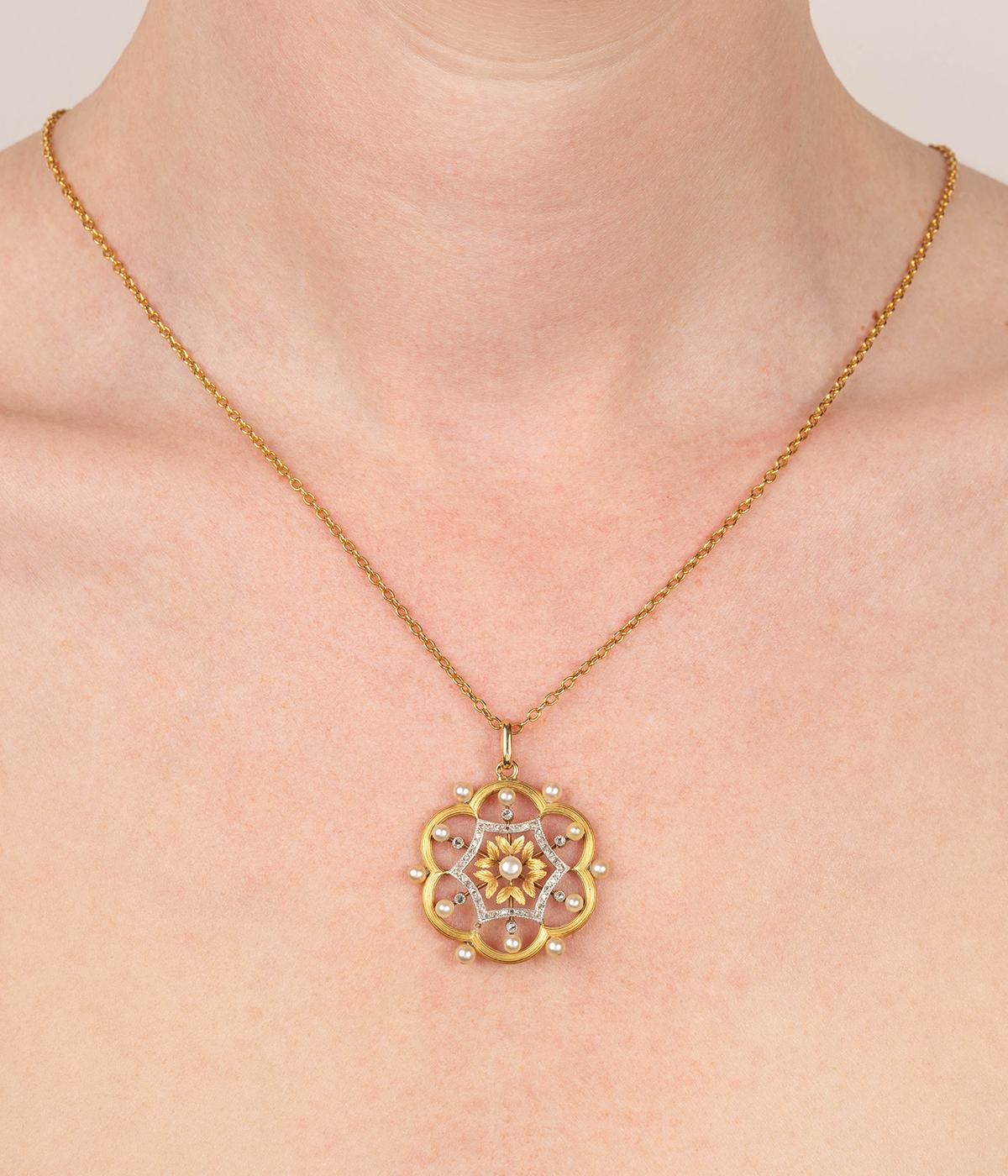Délicat pendentif ancien en or 18 carats (750 millièmes) deux tons du début du 20ème siècle, formant une rosace ajourée et ornée de petites perles et de diamants taille rose.