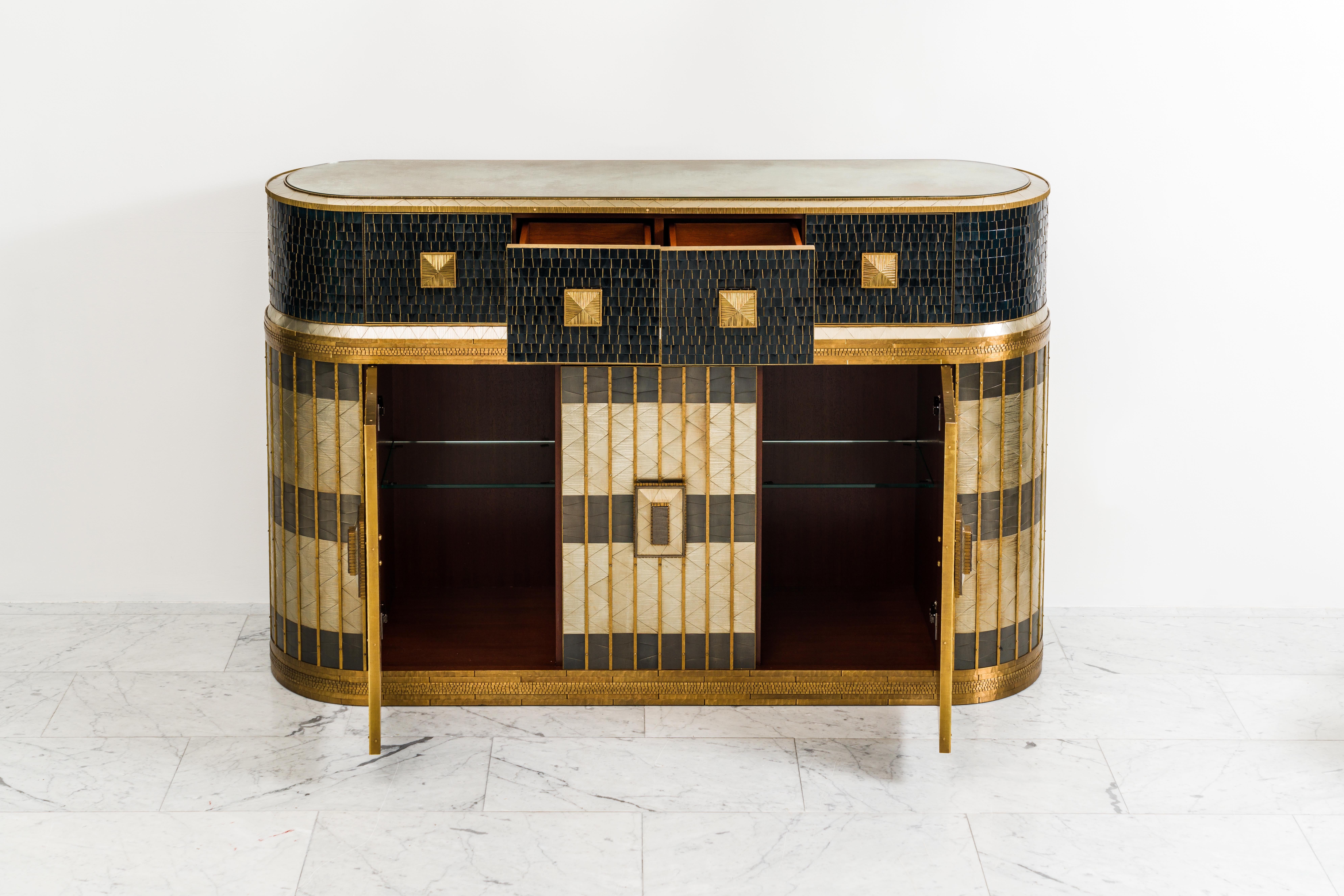 The meticulous craftsmanship and extravagant detailing of Damian Jones's magnificent capsule shaped Penderyn Bar/Highboy Server is a testament to the artist's unique vision.  The two-tiered cabinet is sheathed in a mix of patterned applications of