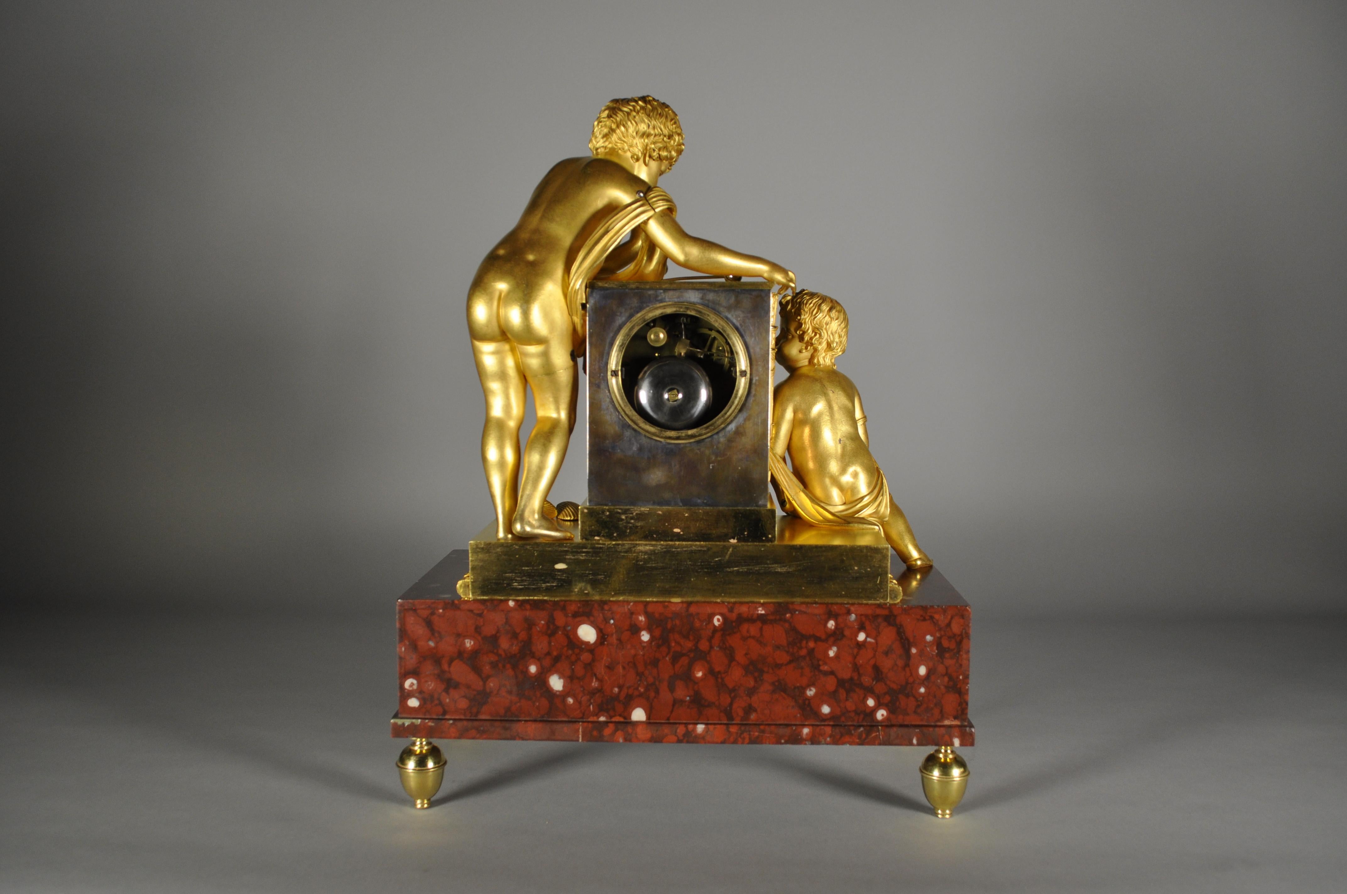 Elegante pendola da tavolo con cassa di alta qualità in bronzo dorato rappresentante due putti che giocano con bolle di sapone su base in marmo rosso griotte. Soggetto molto raro. L'orologio è racchiuso all'interno di un parallelepipedo in bronzo