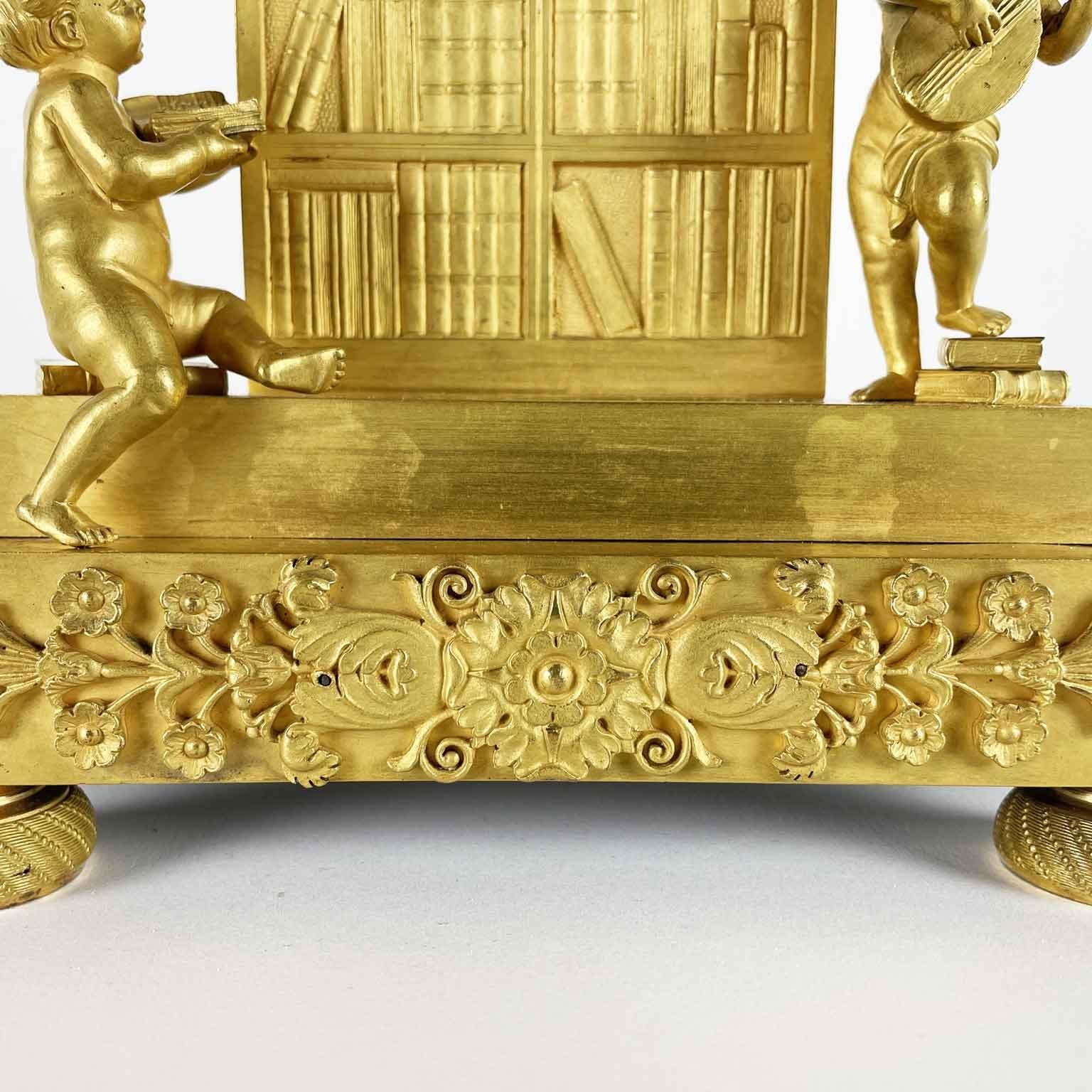 French Empire gilt bronze pendulum dating from the early 1800s,  charming table clock with allegory of the Arts, arched case, flanked by two putti, one seated with a book and the other upright, one foot resting on books, intent on playing a musical